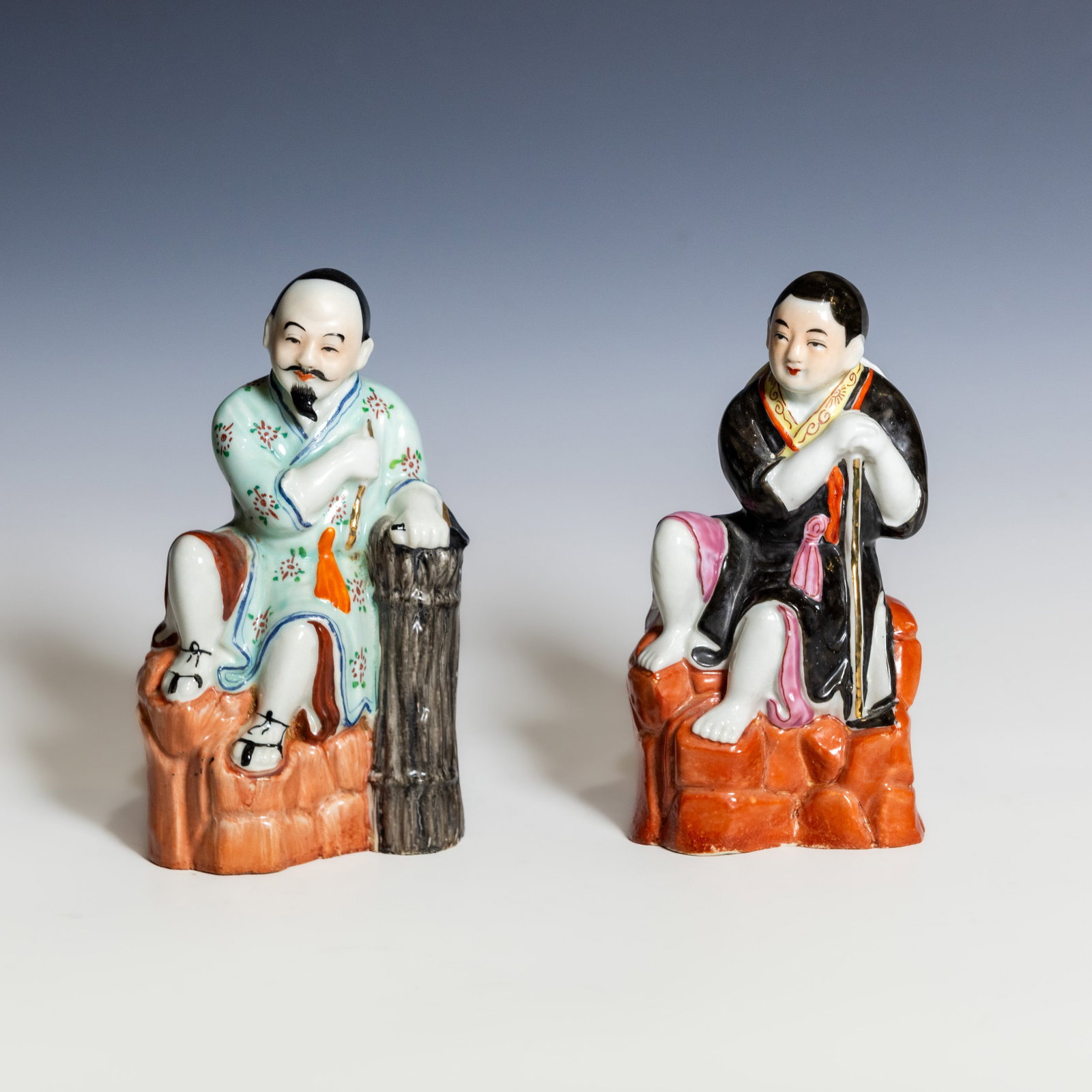 (LOT OF 2) A PAIR OF CHINESE FAMILLE-ROSE PORCELAIN FIGURES WITH MARK: (lot of 2) A pair of Chinese famille-rose porcelain figures. Each is modeled as a seated figure in colorful famille-rose enamels, one depicting a bearded gentleman in a pale turquoise robe leaning aga