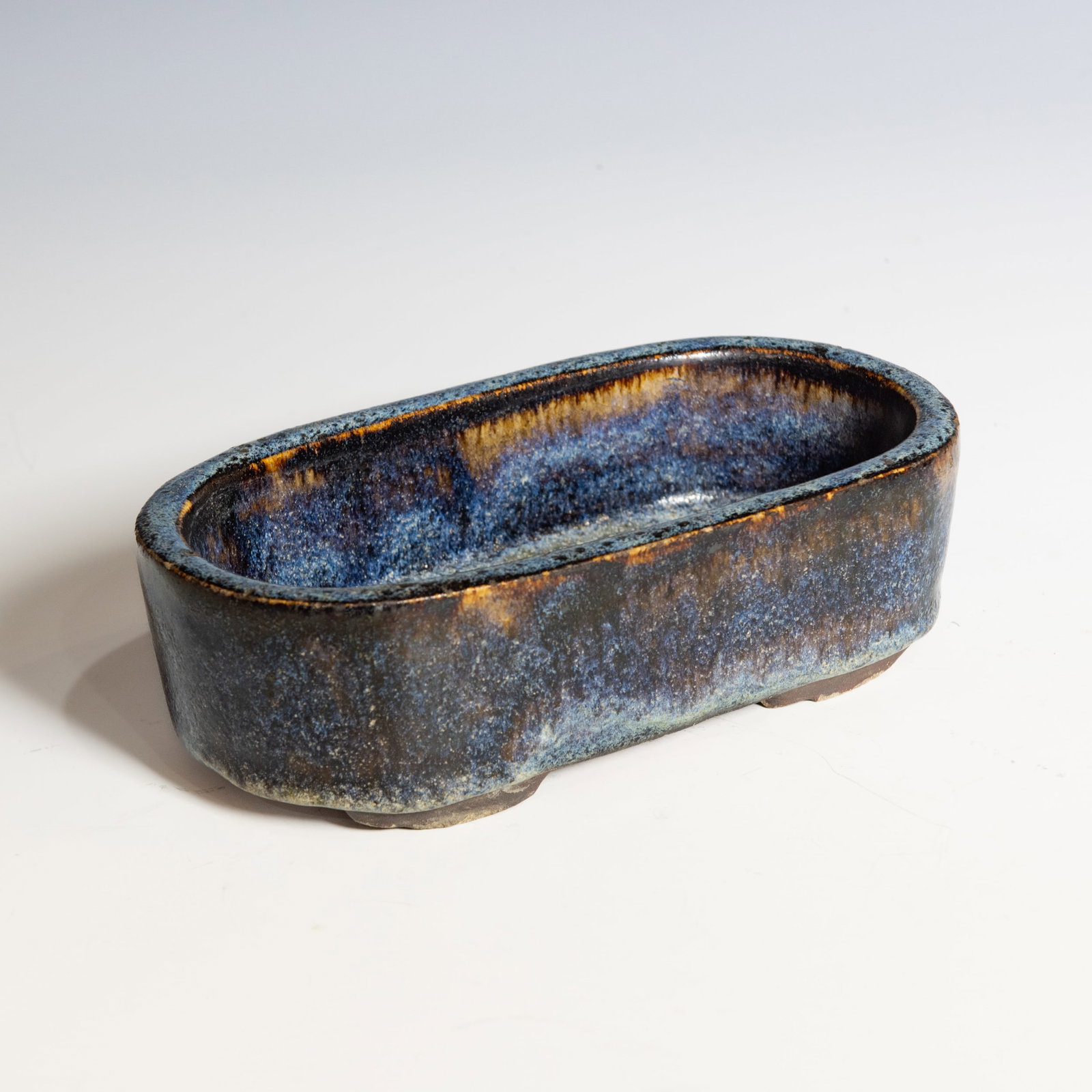 A SHIWAN FLAMBE-GLAZED OVAL VESSEL WITH MARK, QING DYNASTY: A Shiwan flambe-glazed oval vessel with mark, Qing dynasty. The oval-form vessel is covered overall in a rich variegated blue glaze with brown and purple streaking. The interior has a drainage hole