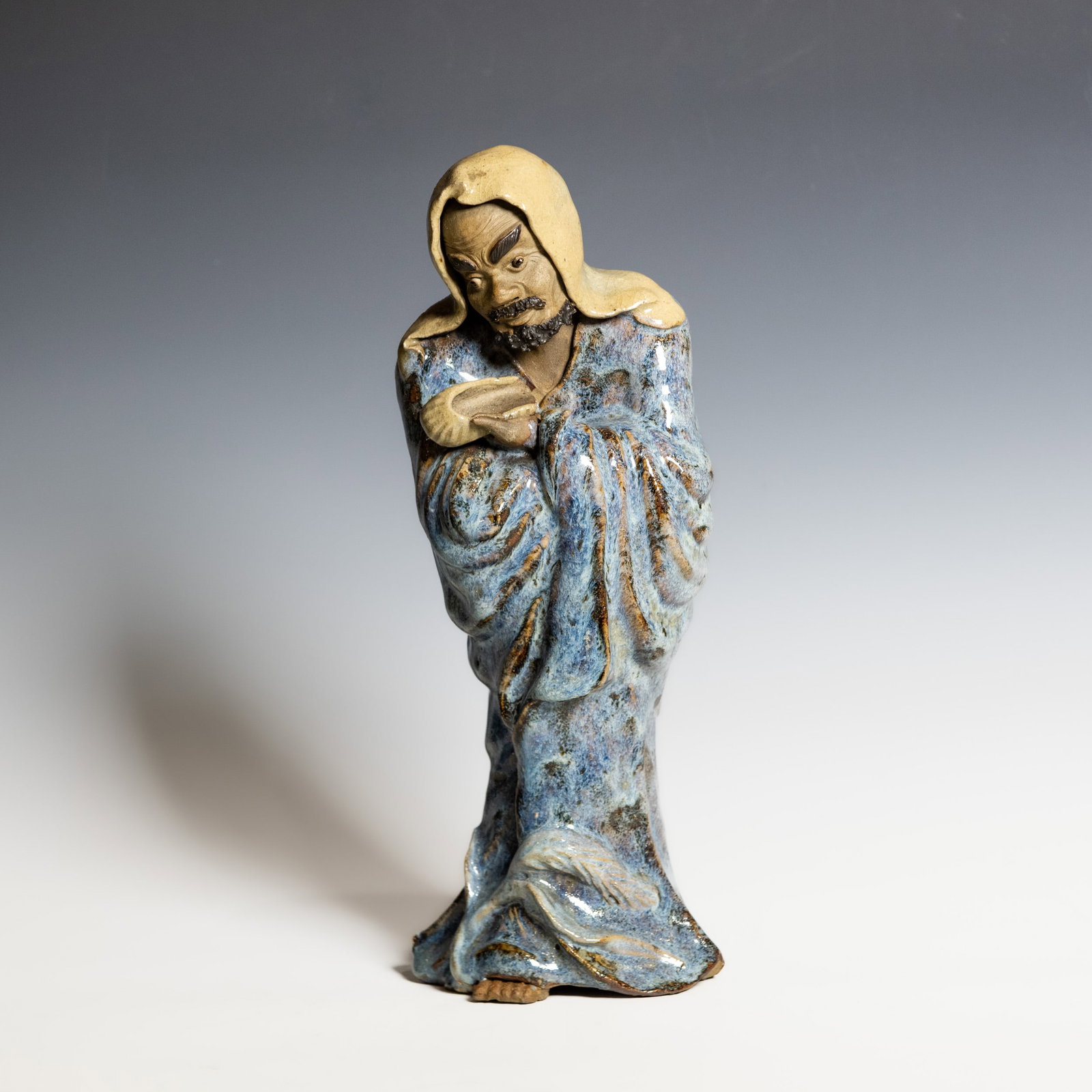 A CHINESE SHIWAN GLAZED FIGURE OF BODHIDHARMA (DAMO), REPUBLIC PERIOD: A Chinese Shiwan figure of Bodhidharma (Damo), Republic period, portrayed standing with a slightly leaning posture, the head covered by a hooded cloak. The figure is rendered with expressive facial