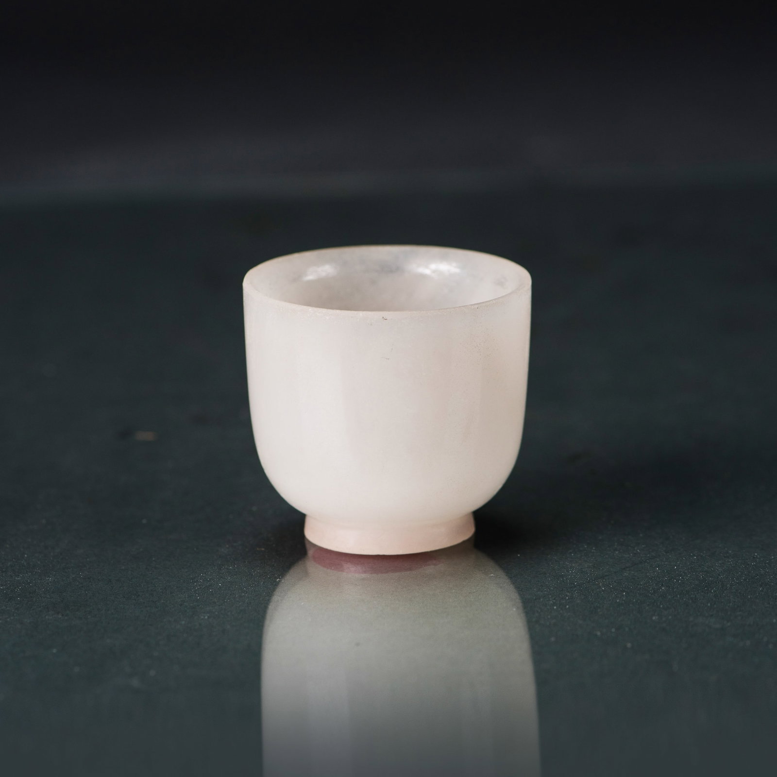 A CHINESE WHITE JADE WINE CUP: A Chinese white jade wine cup with tall sides rising from a short straight foot, smoothly carved and entirely plain. The semi-translucent stone is of a pale tone. 1.85"h x 1.97"w (4.7 x 5 cm)