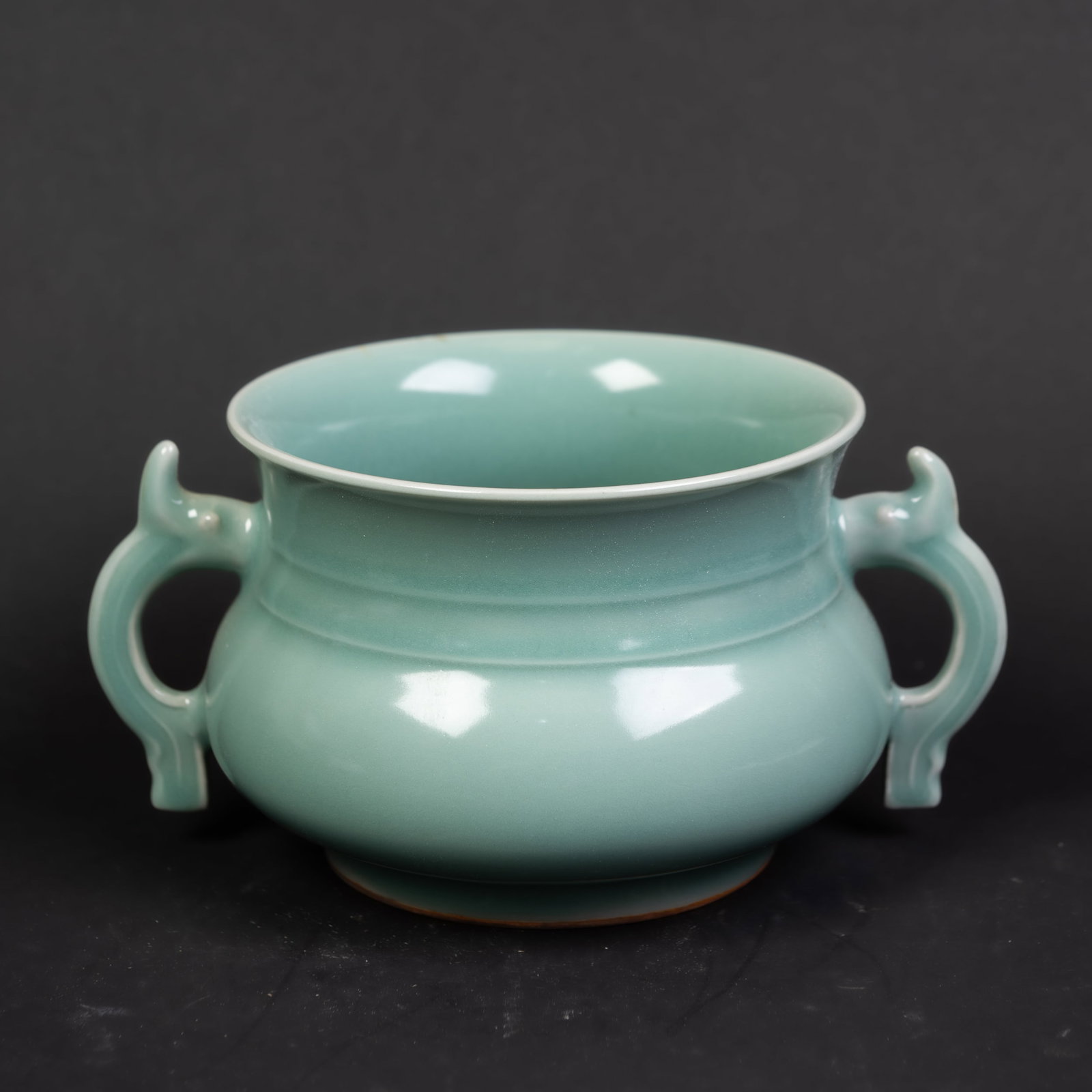 A CELADON PORCELAIN CENSER: A celadon porcelain censer with a compressed rounded body rising to an everted mouth rim, flanked by a pair of handles at the neck. 7.5"h x 4.5"d