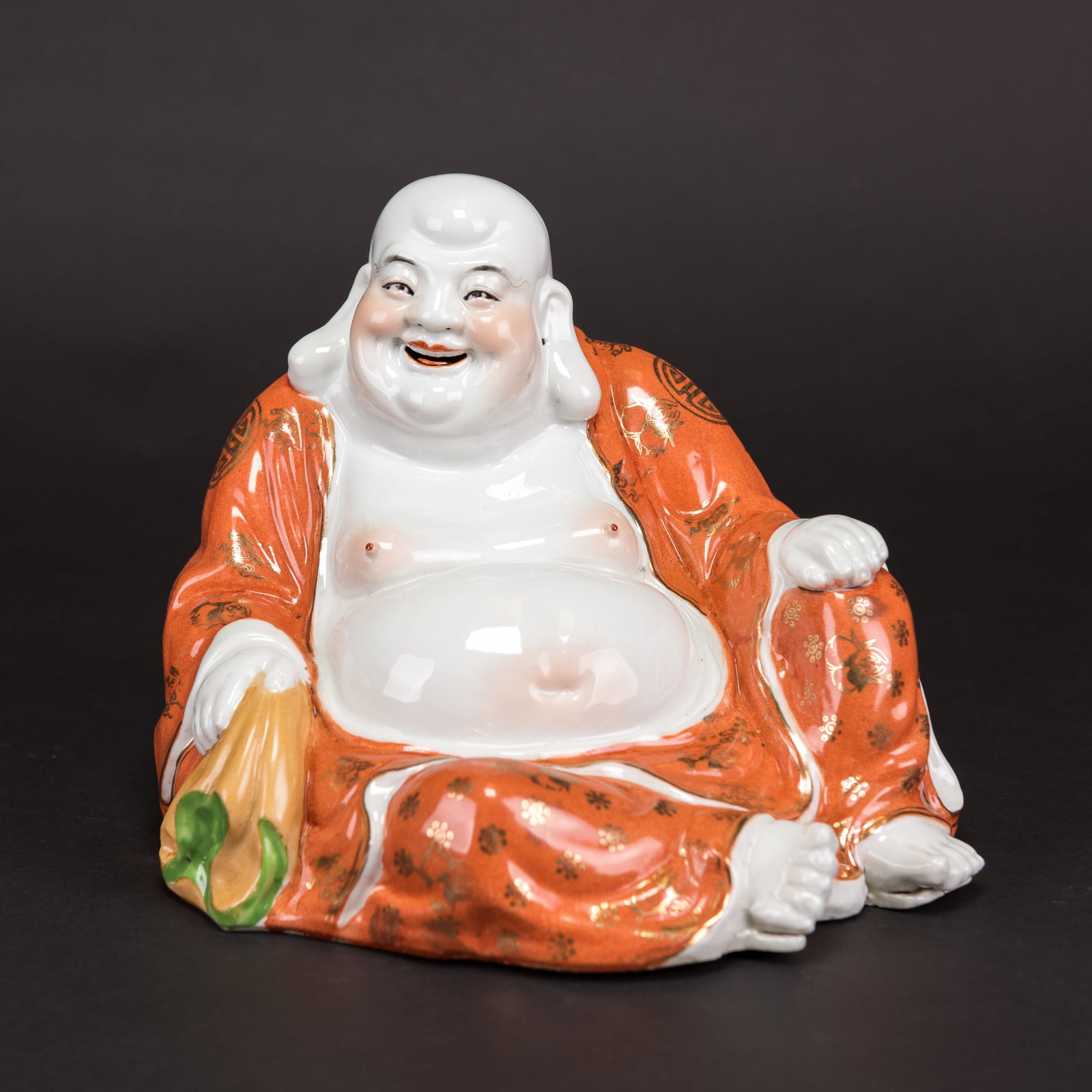 A SMILING BUDDHA STATUE: A smiling Buddha statue in a leaning posture with the feet close together and the hands resting on the knees. H21 x 23.5 x 19 cm