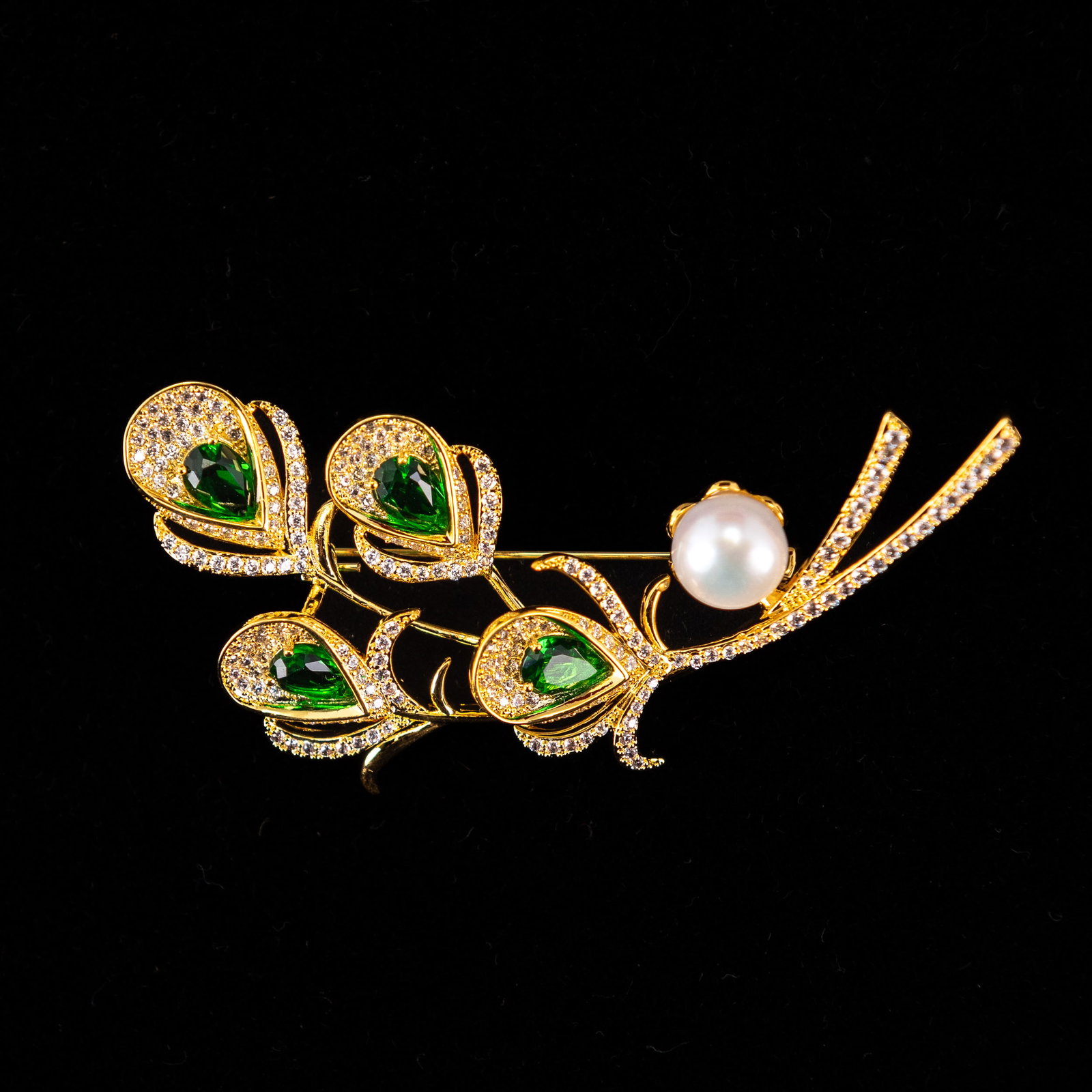 A FASHION JEWELRY EMERALD BERYL-STYLE PEARL BROOCH: A fashion jewelry emerald beryl-style brooch in the form of a feather, with a pearl in the center. 5 x 6.5 cm
