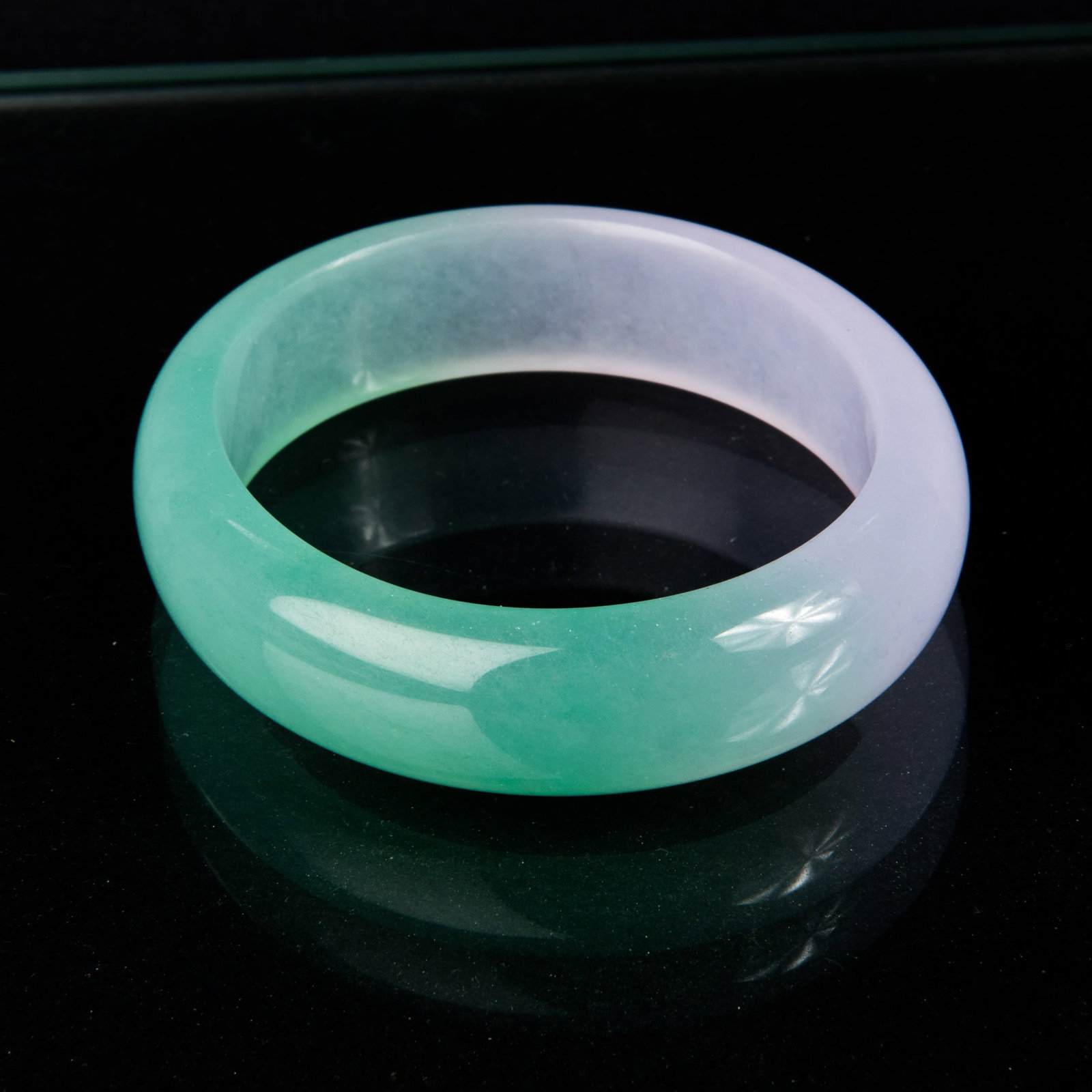 JADEITE BANGLE BRACELET: A highly polished translucent jadeite bangle bracelet, half icy green and half light lavender. 0.5"h x 2.5"w x 2.75"l (1.27 x 6.35 x 6.99 cm)