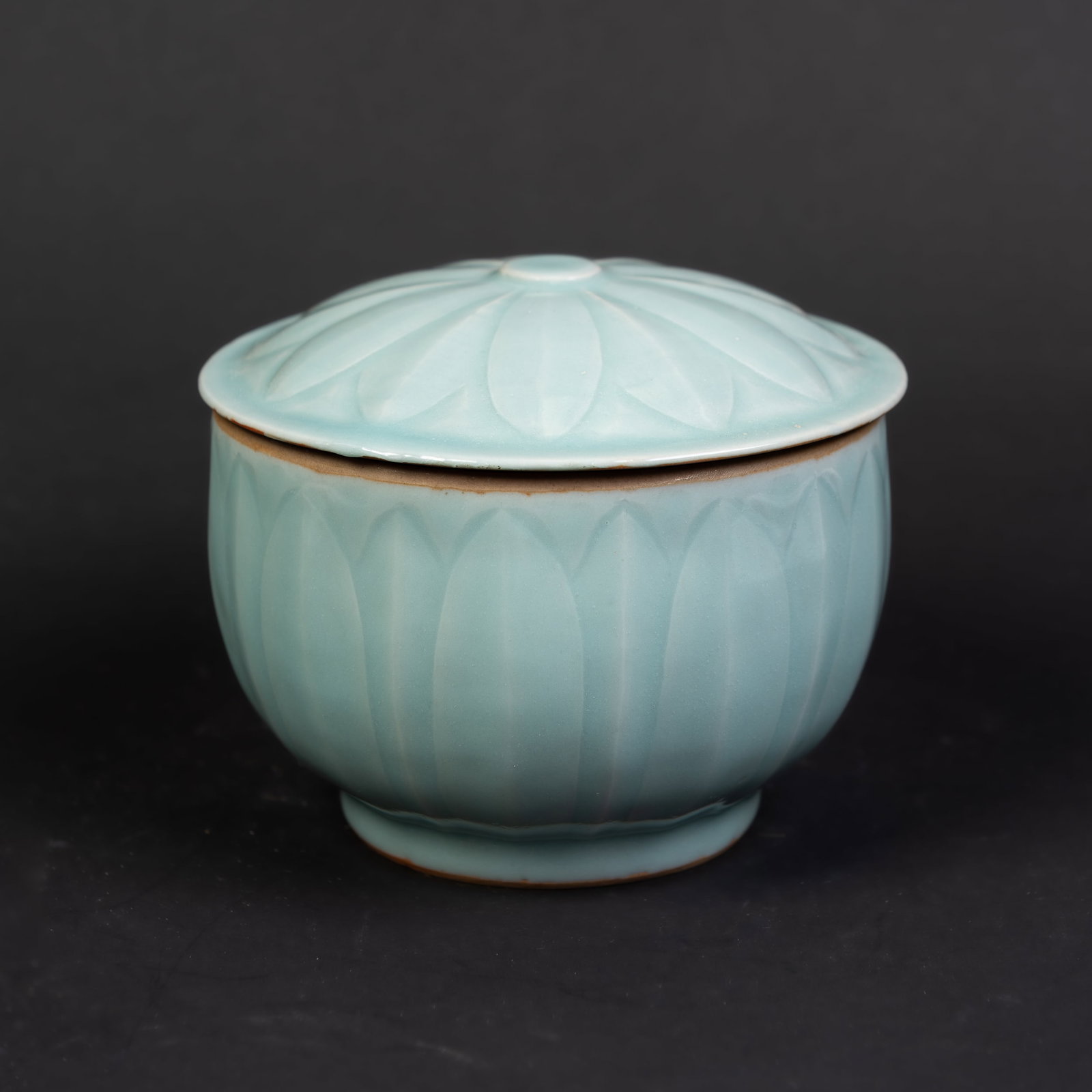A CELADON PORCELAIN JAR: A celadon porcelain jar of rounded form, carved with a flower-petal pattern and with a lid. 5.25"h x 5.75"d