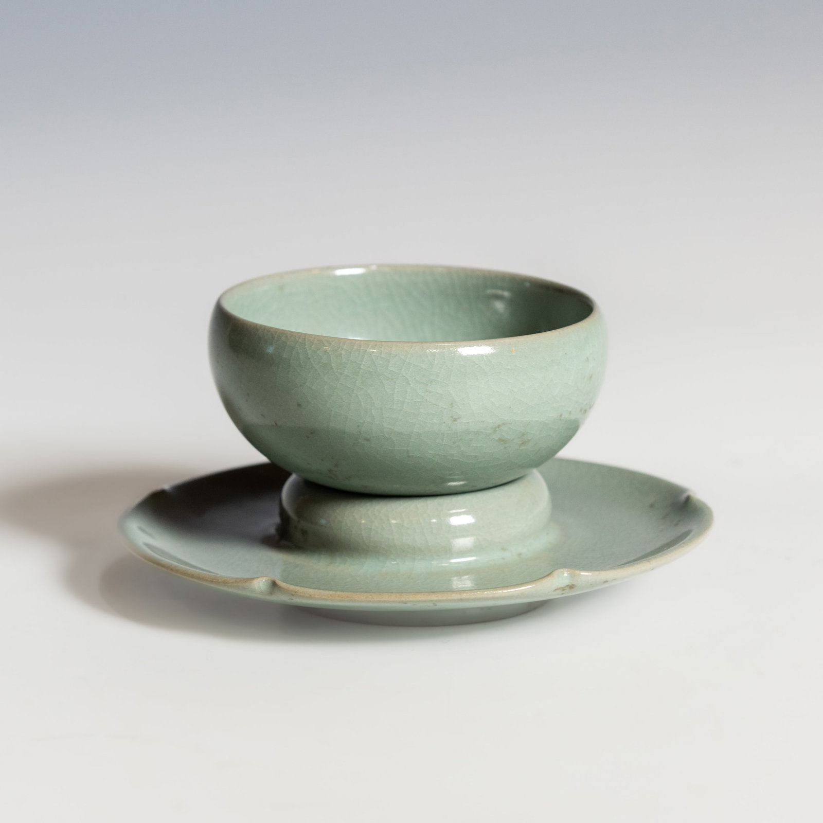 A CELADON-GLAZED BOWL AND STAND: A celadon-glazed bowl and stand, both covered overall with a crackled glaze of soft green tone, the bowl with rounded sides resting on a slightly splayed foot. Bowl: 1.77"h x 3.15"d (4.5 x 8 cm);