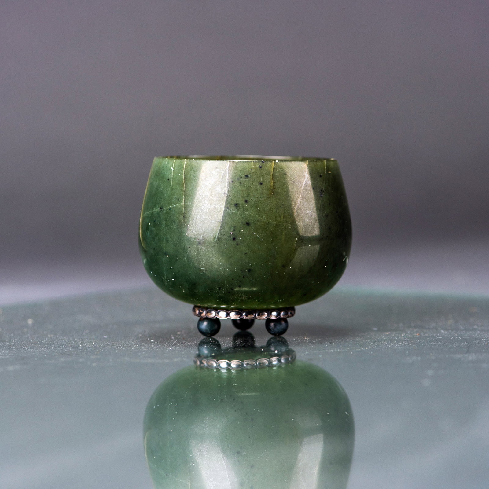 A SPINACH JADE CUP: A spinach jade cup with deep rounded sides rising from a short straight foot, the semi-translucent stone of a spinach tone. H6 x 6.5 cm