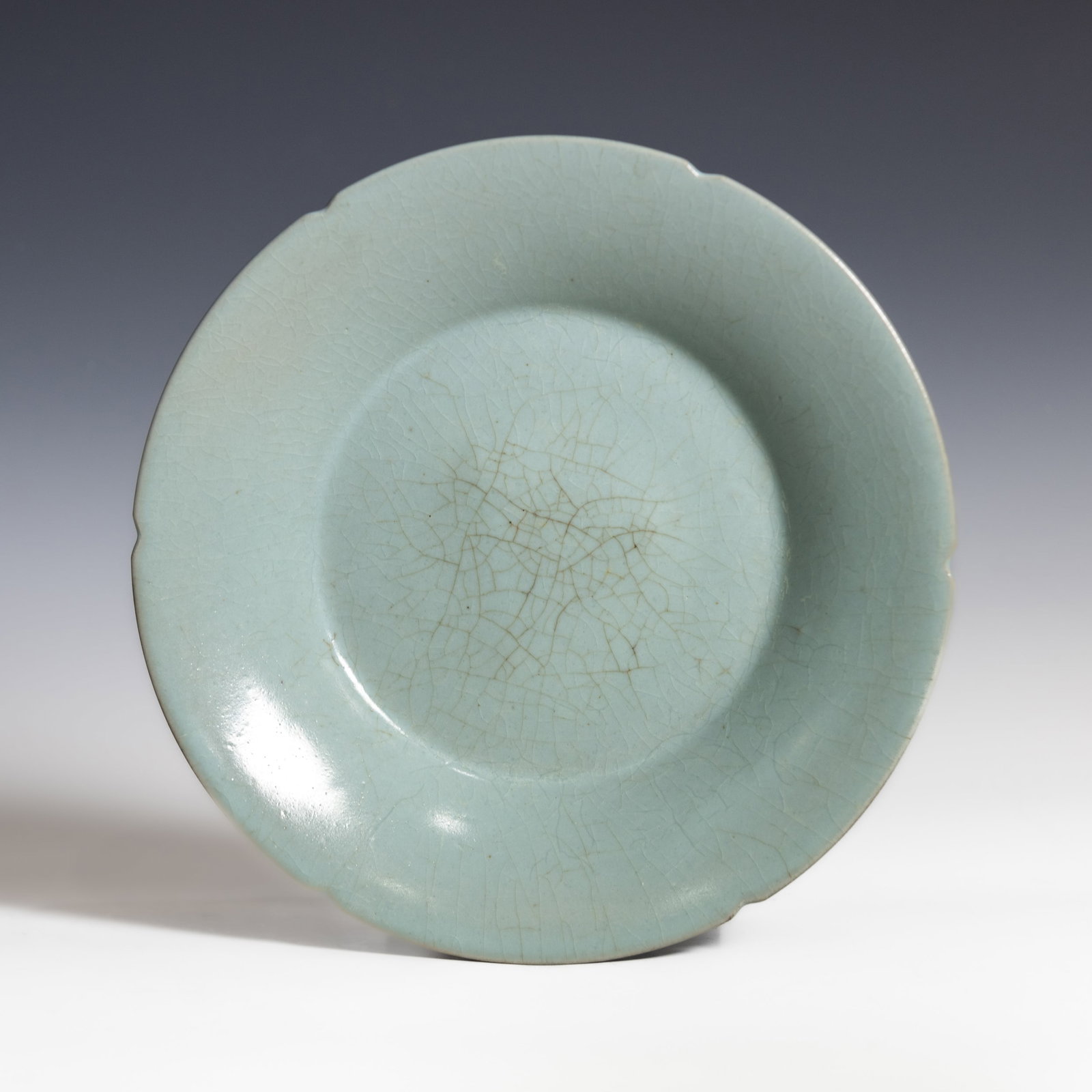 CHINESE CELADON-GLAZED DISH: Chinese celadon-glazed dish with shallow rounded sides rising to a slightly everted rim, covered overall in a celadon glaze suffused with a network of crackles. The rim has shallow notches forming a