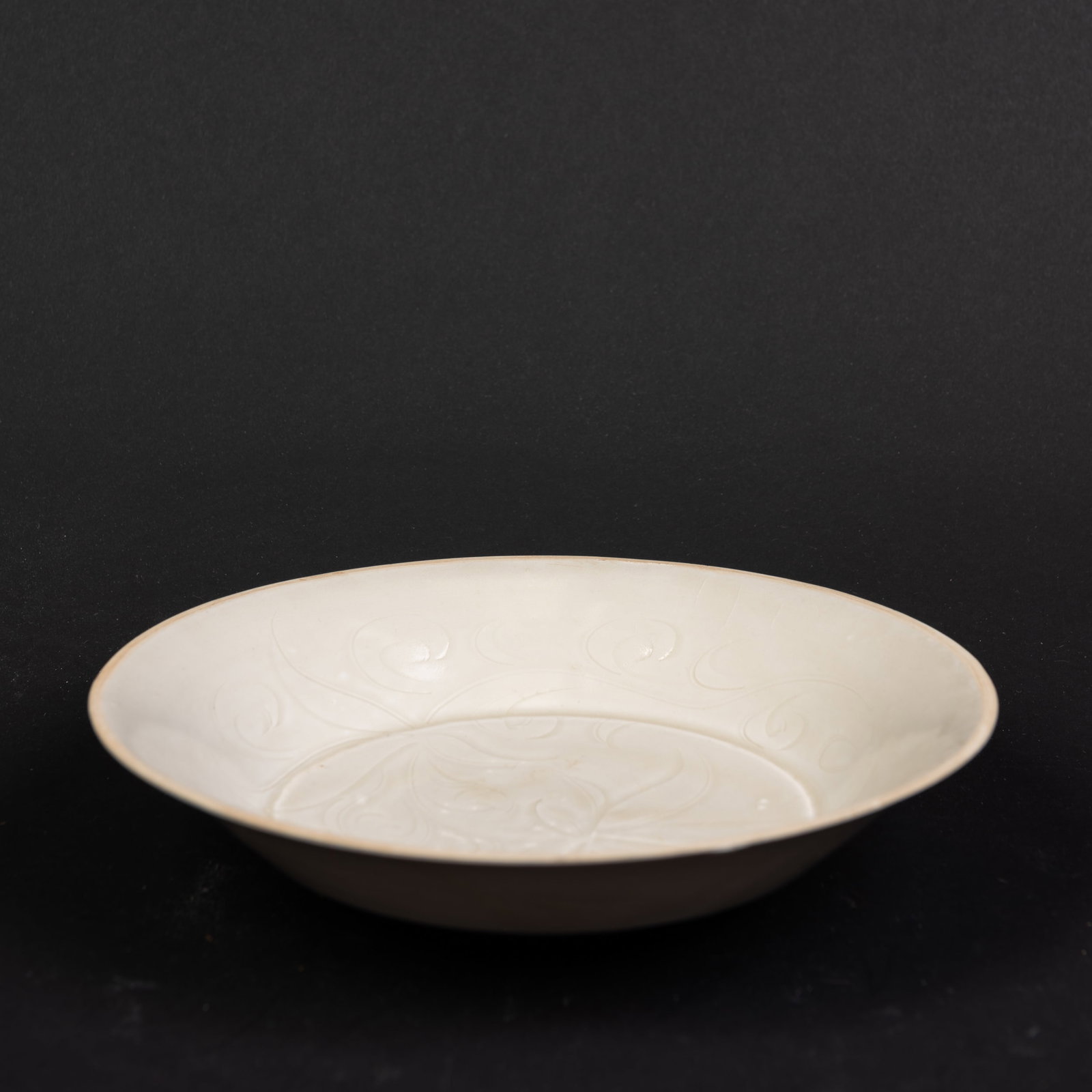 A WHITE-GLAZED PORCELAIN DISH: The dish has rounded sides rising to an everted rim and is covered overall with an even white glaze. The interior is carved with a decorative pattern. 2"h x 7.75"d