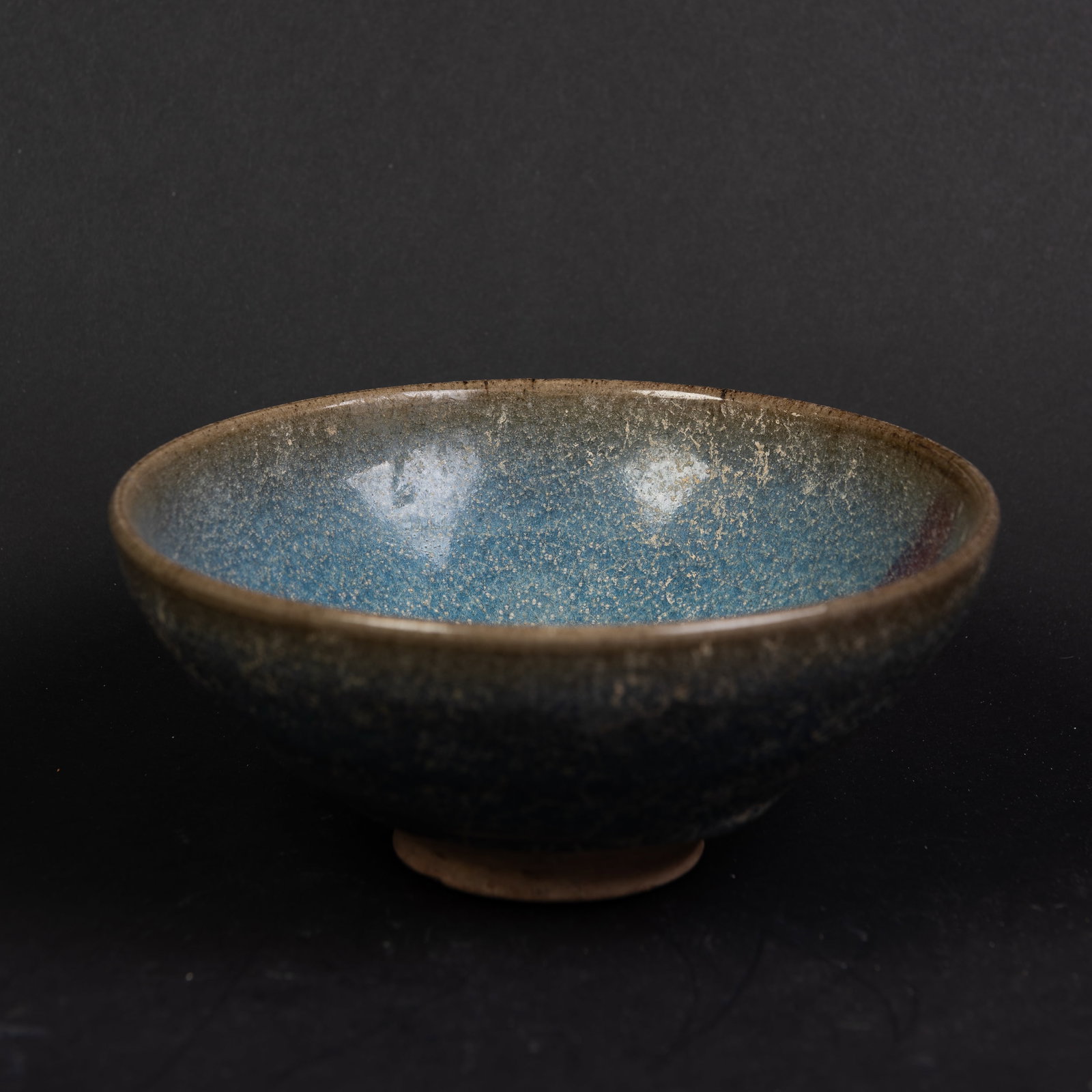 A CHINESE JUNYAO BOWL: A Chinese Junyao bowl of conical form with a slightly inverted rim, covered on the interior and exterior with a thick crackled glaze of milky lavender tone with purple splashes, falling slightly short