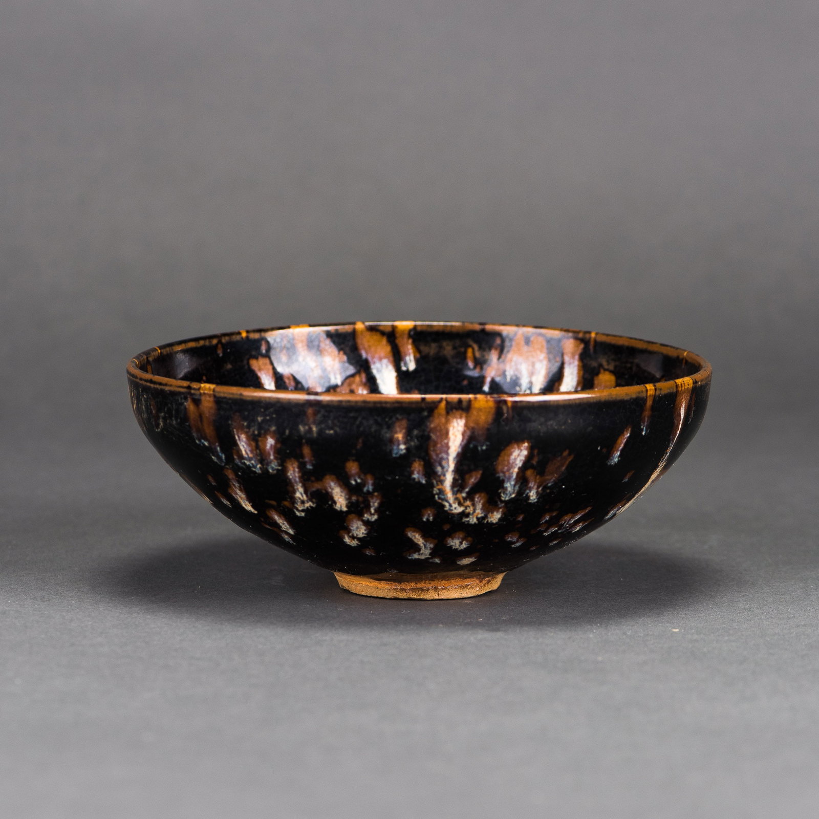 A TENMOKU TEA ZHAN: A Tenmoku tea zhan with deep rounded sides, covered inside and out with a thick iridescent black glaze suffused with a dense pattern of variegated iridescent oil spots. H6.5 x 15.7 cm
