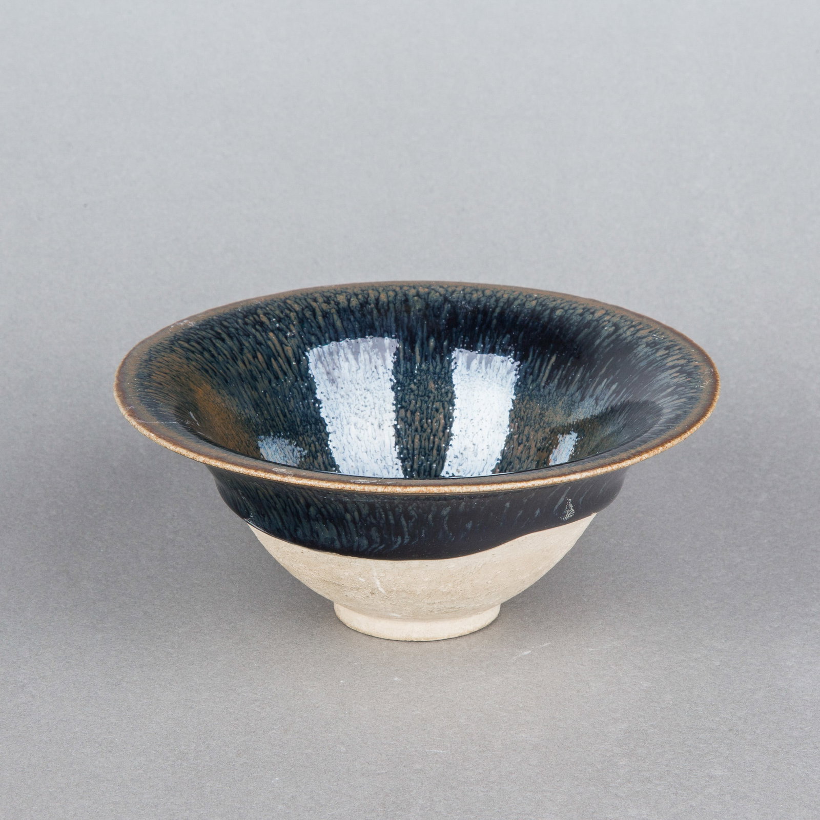 A JIAN TEA BOWL: A Jian tea bowl with deep sides rising to a flared rim, covered inside and out with a thick iridescent black glaze. H5.5 x 14 cm