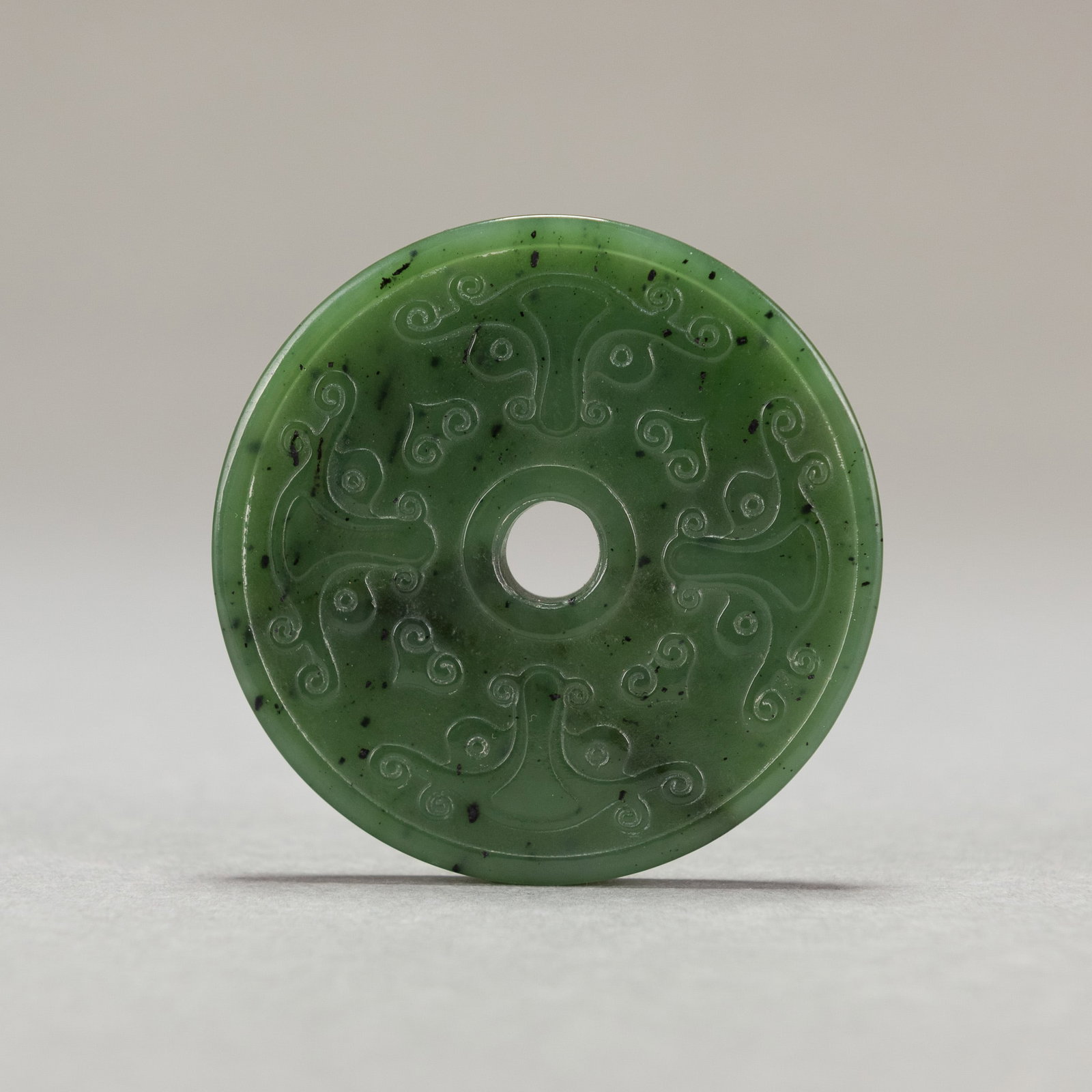 GREEN JADE BI DISC PENDANT: Green jade bi disc pendant, carved in relief on both sides with decorative patterns. 2.56"d x 0.16"w (6.5 x 0.4 cm); 29.6 dwt