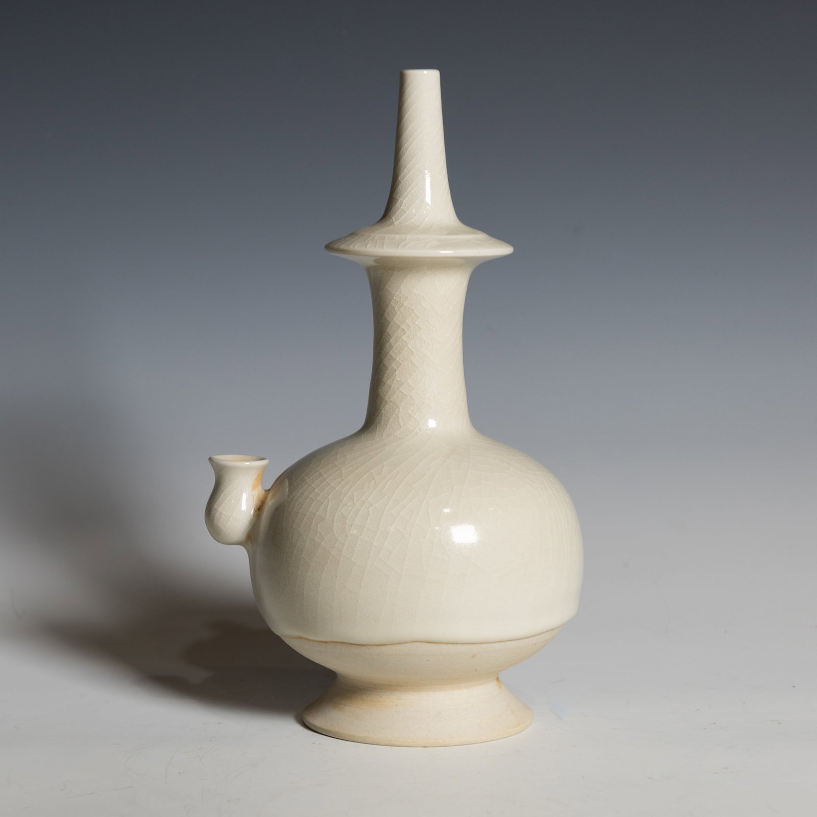 CHINESE WHITE-GLAZED EWER: Chinese white-glazed ewer with a globular body rising from a splayed foot to a tall cylindrical neck surmounted by a flared disc collar and narrow mouth, set with a short spout on the shoulder. The