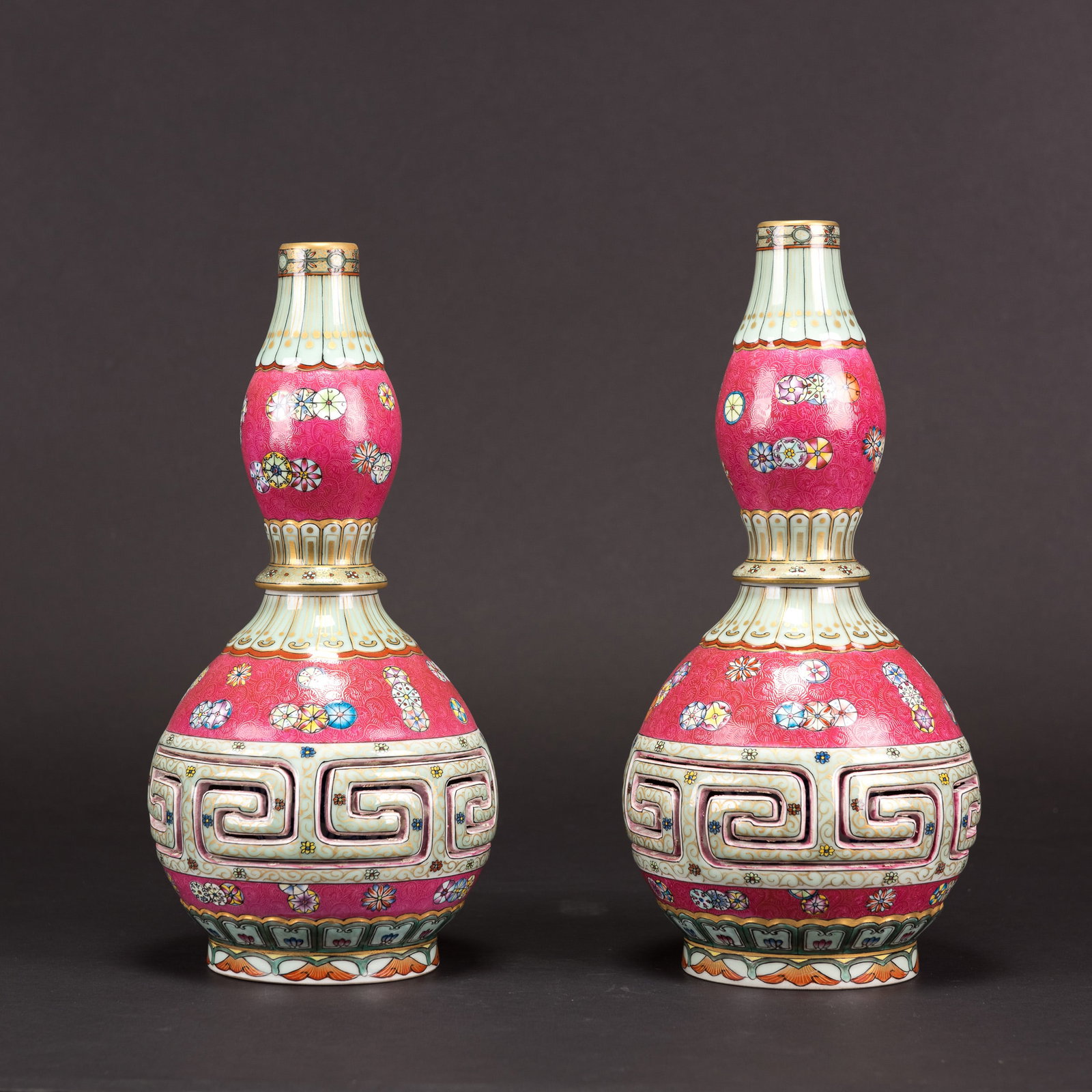 (LOT OF 2) PAIR OF FAMILLE-ROSE DOUBLE-GOURD VASES: (lot of 2) A pair of famille-rose double-gourd vases, each delicately enameled with scattered floral roundels against a vibrant pink ground, the midsection decorated with a band of stylized geometric