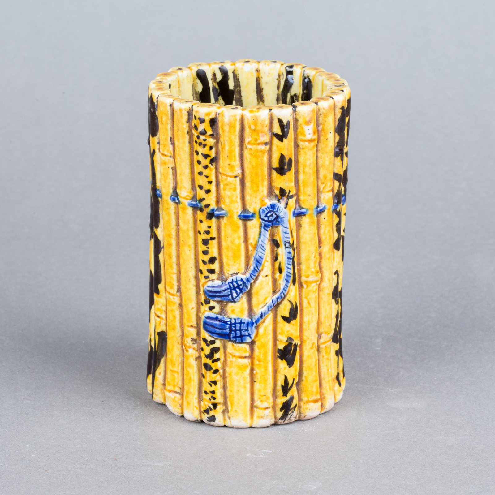 A PORCELAIN 'BAMBOO' BRUSH POT: A porcelain 'bamboo' brush pot. Modeled in the form of bamboo, covered with a yellow glaze and painted with bamboo leaves. 4.33"h x 2.56"d (11 x 6.5 cm)