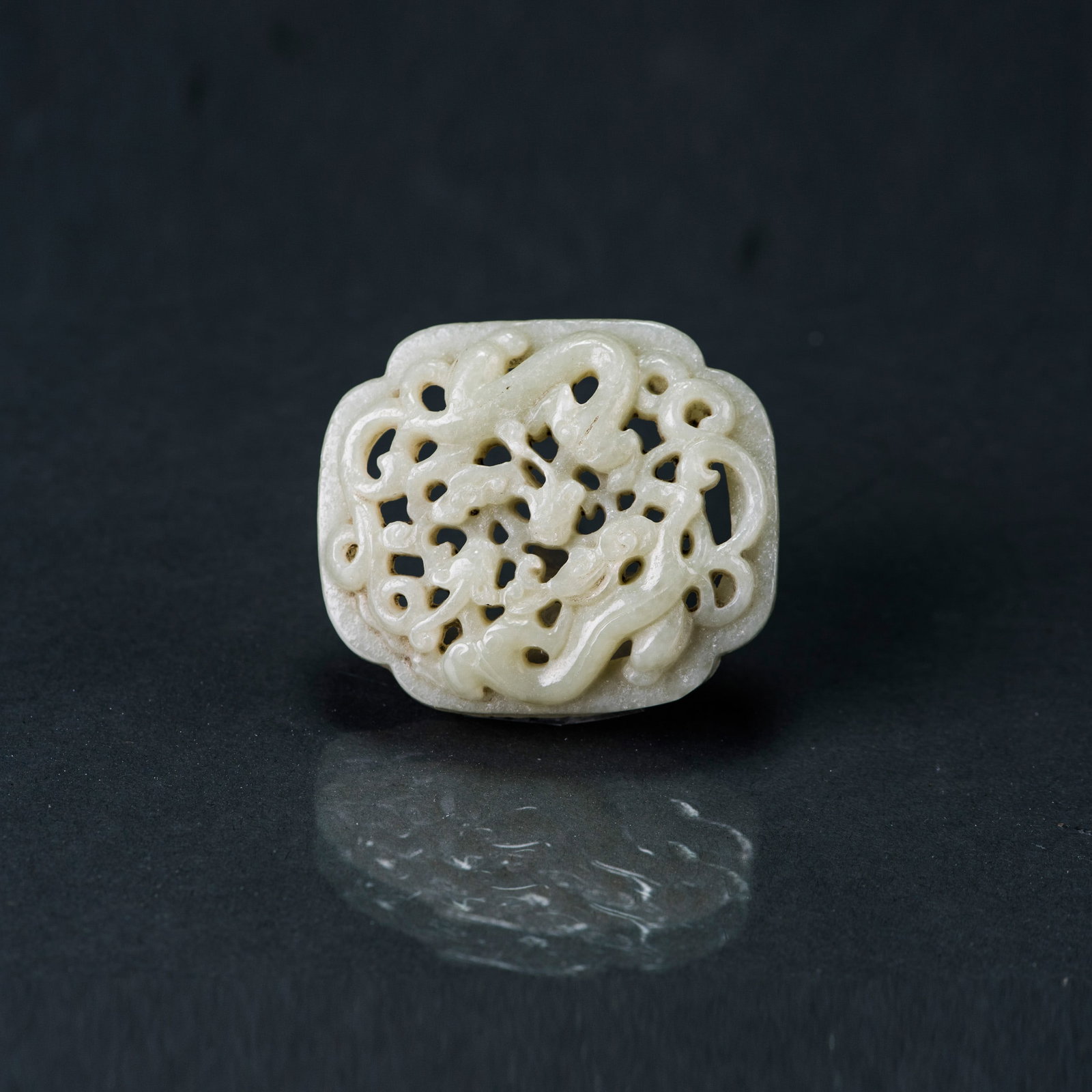 A PALE GREEN JADE RETICULATED 'DRAGON' PLAQUE: A pale green jade reticulated 'dragon' plaque. Of oval domed form, elaborately carved in openwork with a chilong amidst dense scrolling motifs, the stone of a pale green tone. 0.39"h x 2.17"w x