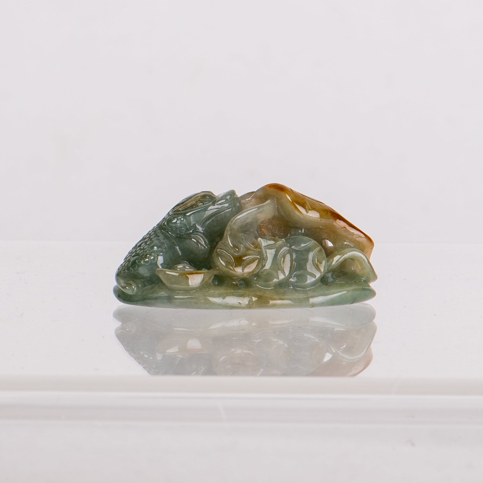 JADEITE CARVING OF CICADA AND LOTUS: Jadeite carving of a cicada and lotus, the stone of a green tone with several russet streaks on the body of the cicada. 1"h x 1.1"w x 2"l (2.54 x 2.79 x 5.08 cm)