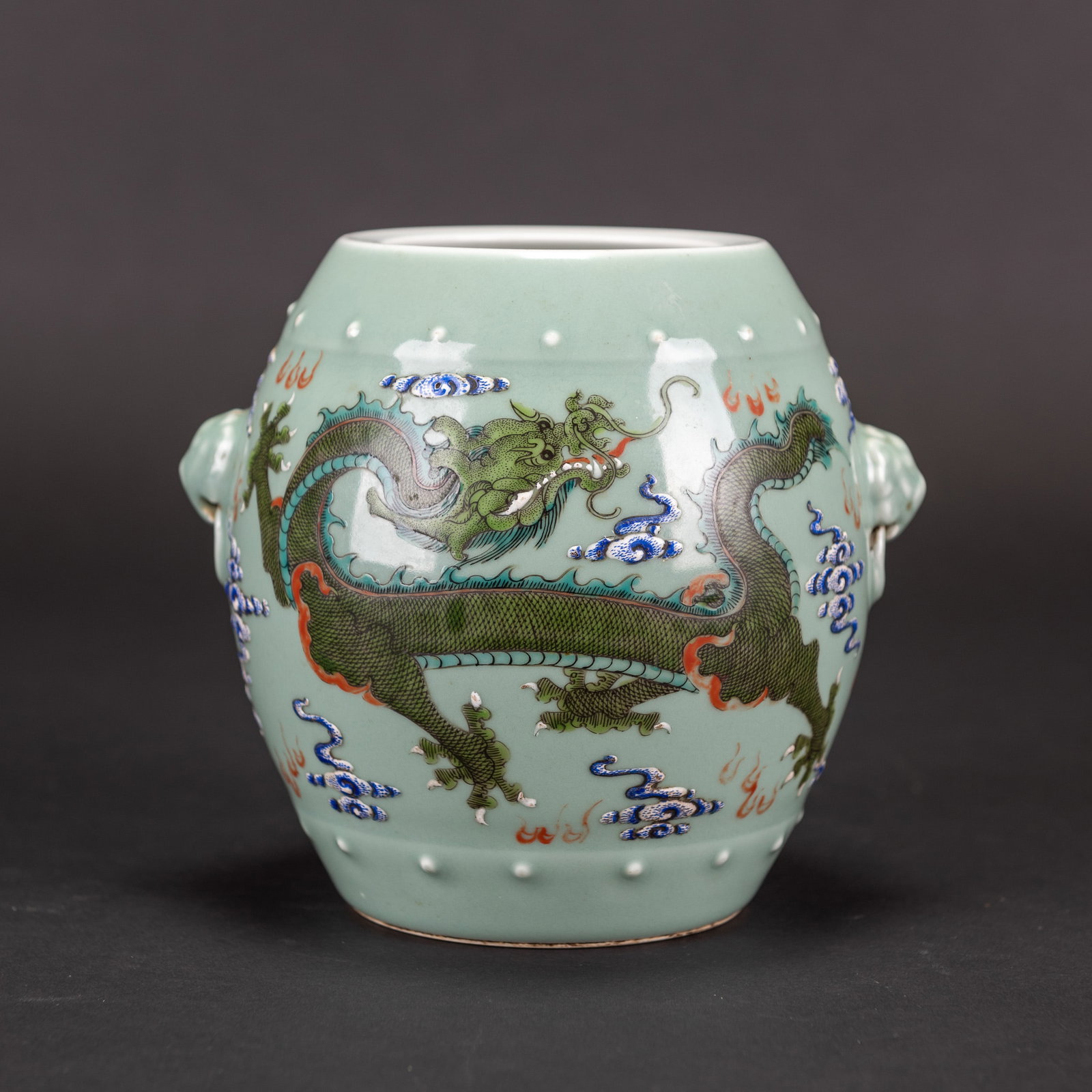 A CELADON-GROUND PORCELAIN JAR DECORATED WITH DRAGONS: A celadon-ground porcelain jar, finely painted with five-clawed dragons striding amidst auspicious clouds and flames, set with applied animal-head handles on each side. H15.5 x 15 cm