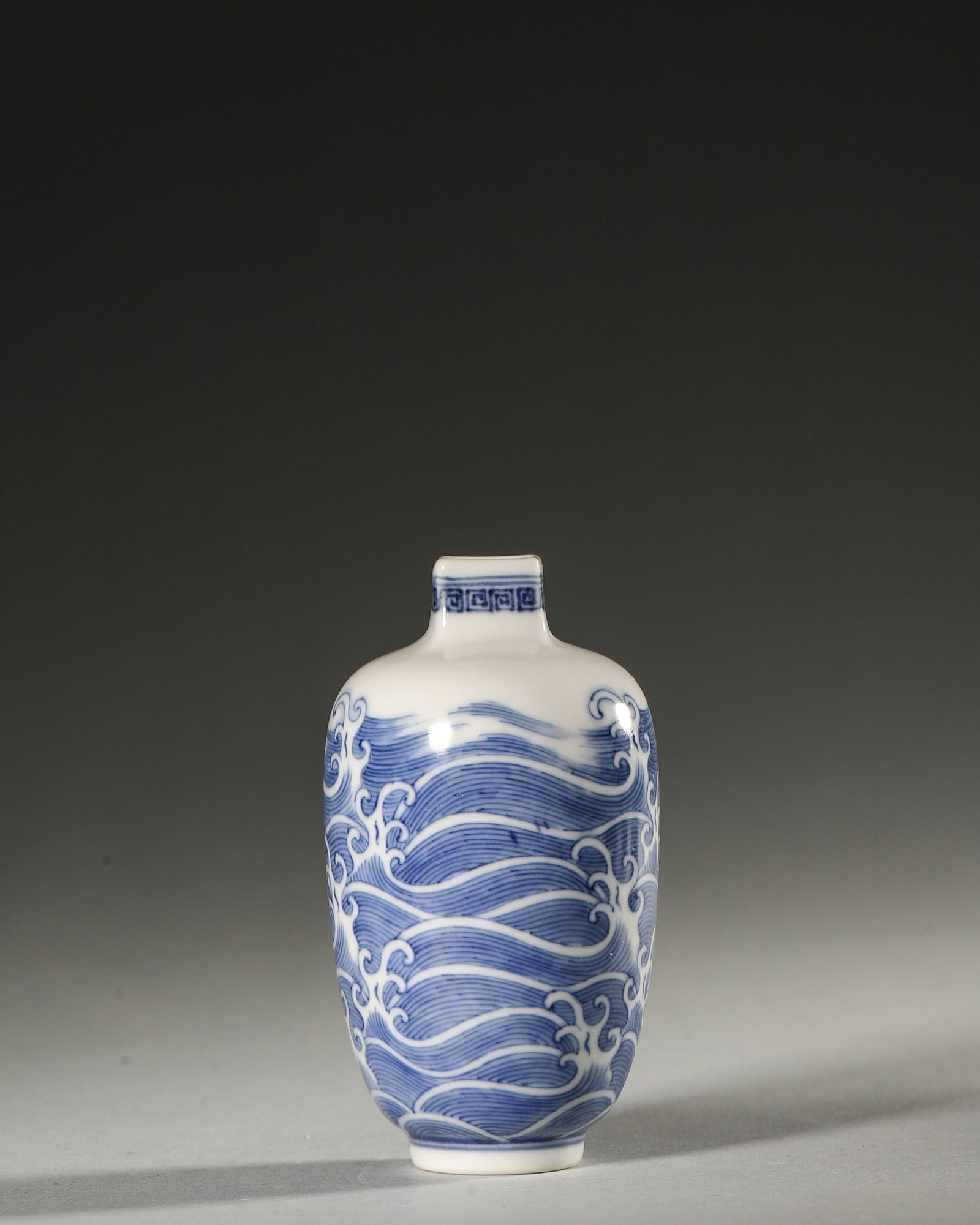 A BLUE-AND-WHITE 'WAVE' PORCELAIN SNUFF BOTTLE: A blue-and-white porcelain snuff bottle decorated with wave motifs. Diam. 5.3 cm; Ht. 8.6 cm.