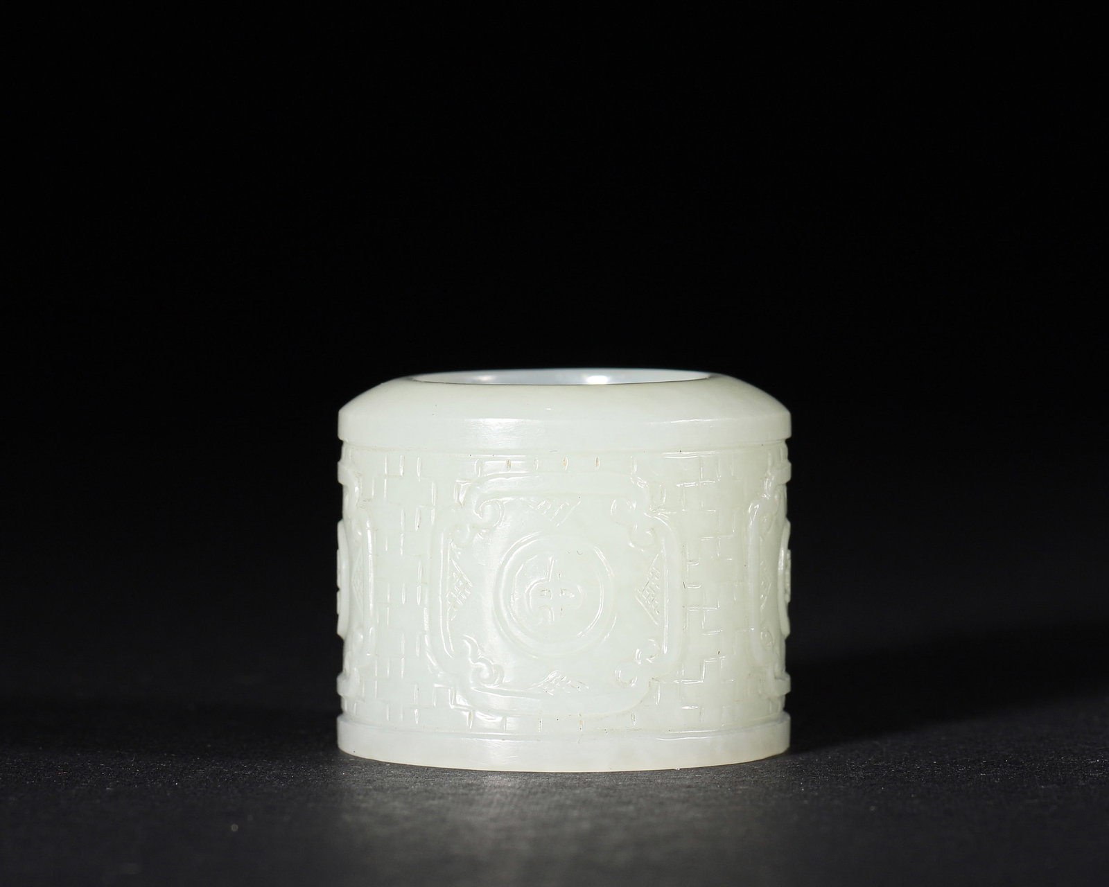 A WHITE JADE THUMB RING WITH BROCADE-PATTERN RELIEF: A white jade thumb ring carved in relief with a brocade-style pattern. Inner Diam. 20 mm; W. 25 mm; Wt. 37 g.