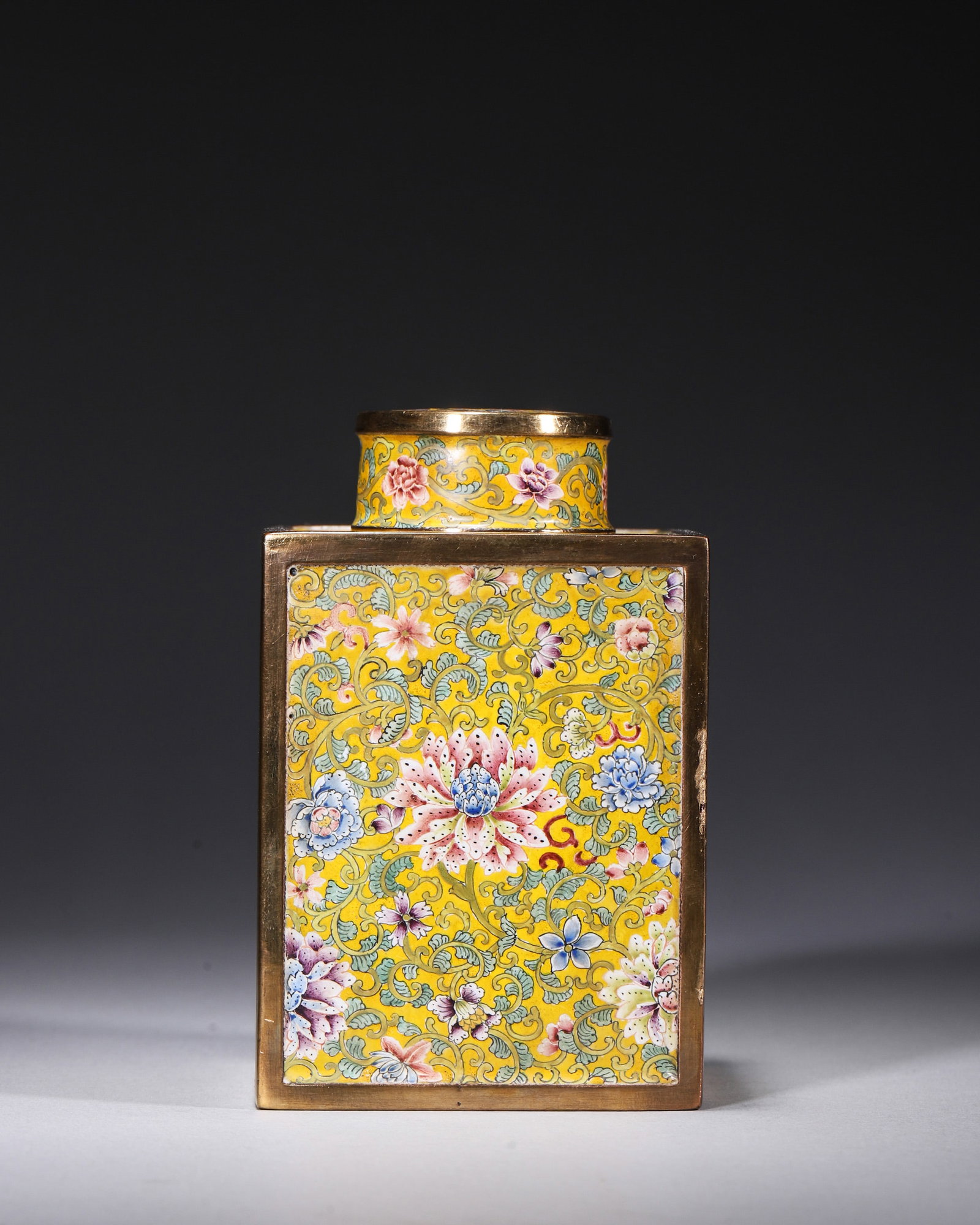 A GILT-BRONZE PAINTED-ENAMEL SQUARE TEA CADDY WITH LOTUS SCROLLS: A square gilt-bronze painted-enamel tea caddy with cover, decorated with lotus scrolls on a yellow ground, with a turquoise interior. The base bears a mark reading 'Qianlong Nian Zhi'. L. 6.5 cm; W. 6