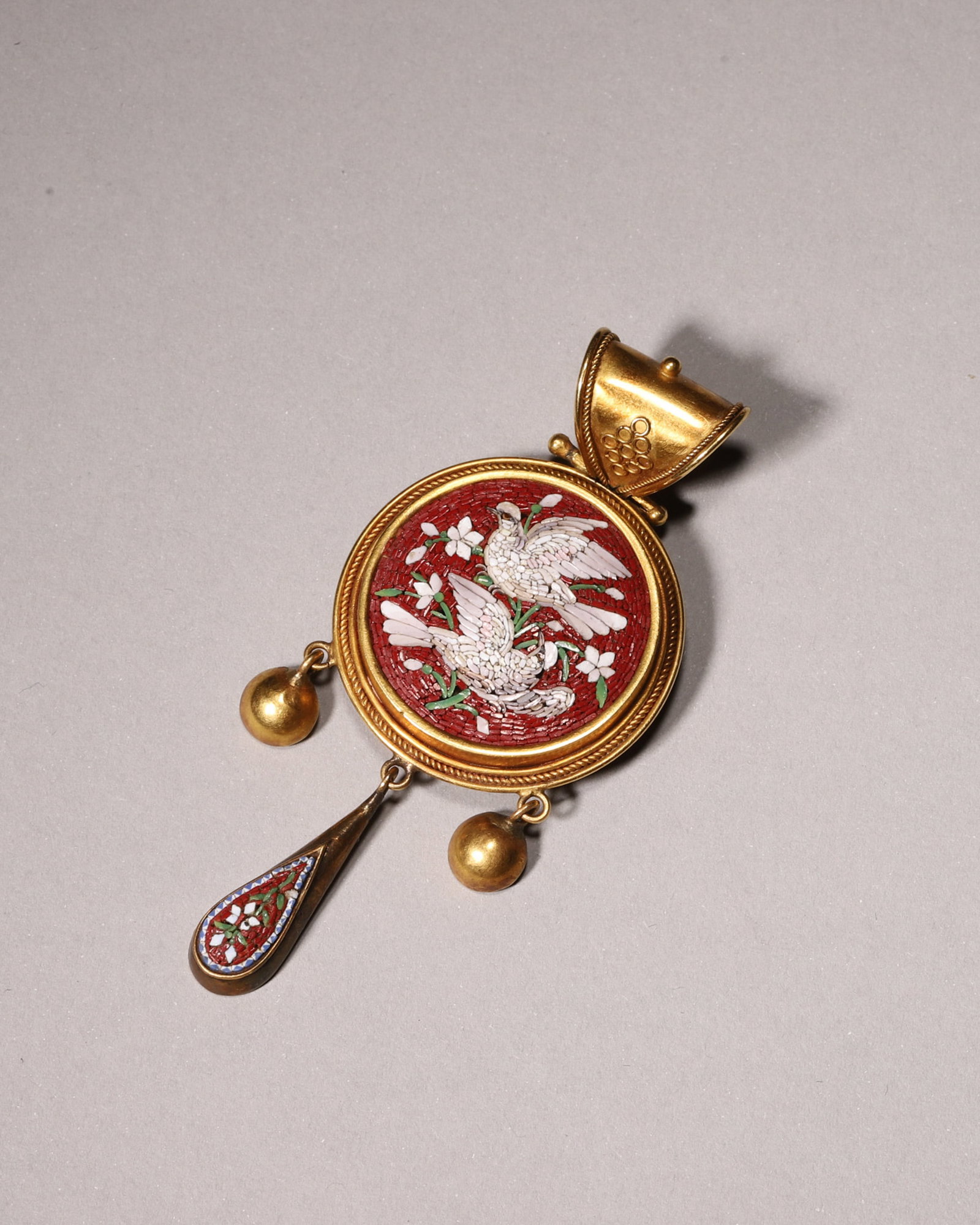 A GOLD ALLOY AND MICROMOSAIC DOVE AND FLORAL PENDANT: A gold-alloy pendant set with micromosaic decoration depicting two doves and flowers on a red ground, with suspended gold-alloy beads and a teardrop-form micromosaic drop. L. 6 cm; W. 2.7 cm; Wt. 14