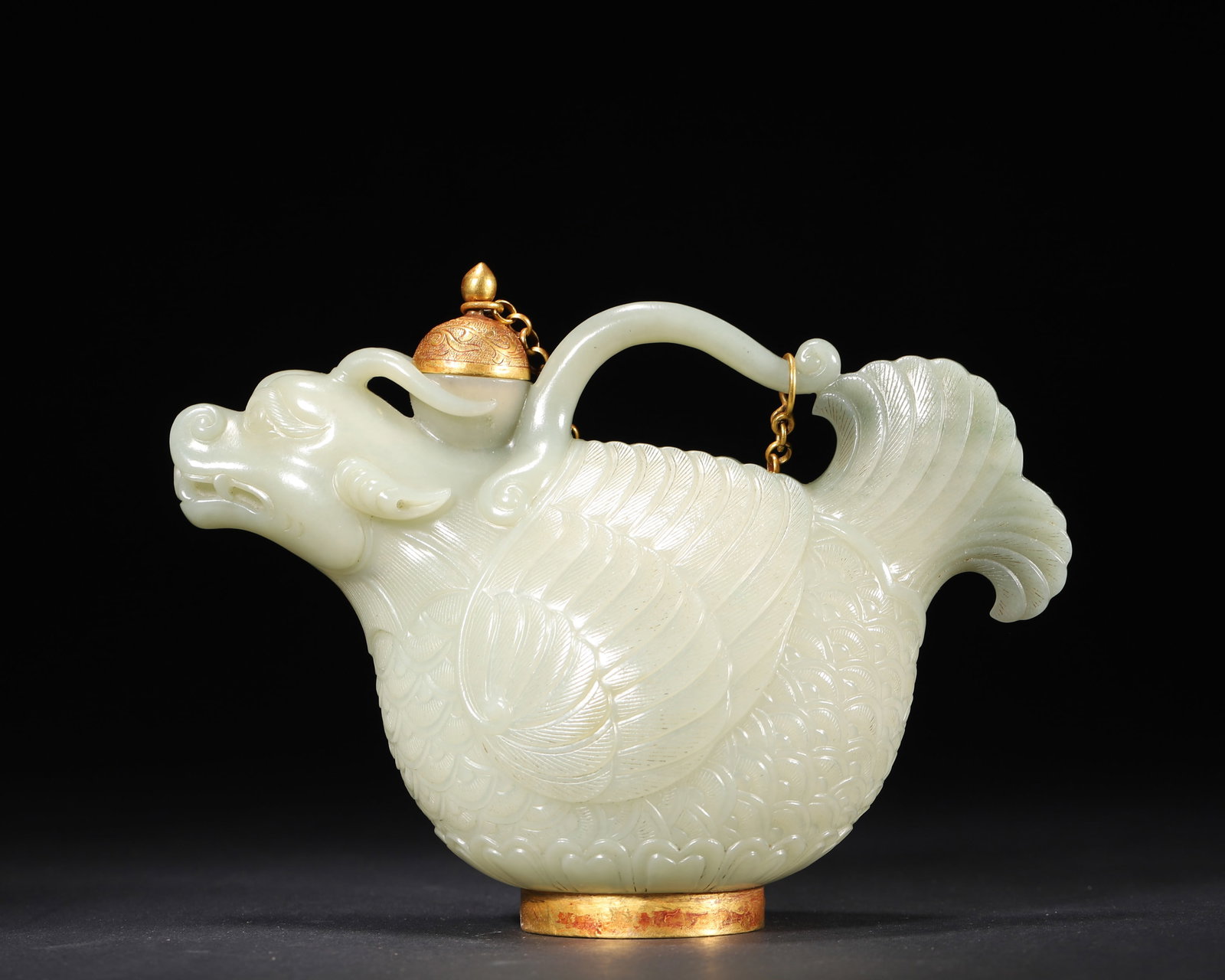 A WHITE JADE GILT 'FISH-DRAGON' EWER: A white jade ewer carved with a fish-dragon form and gilt decoration, with incised scale and feather details. L. 17 cm; W. 7 cm; Ht. 13 cm; Wt. 219 g.