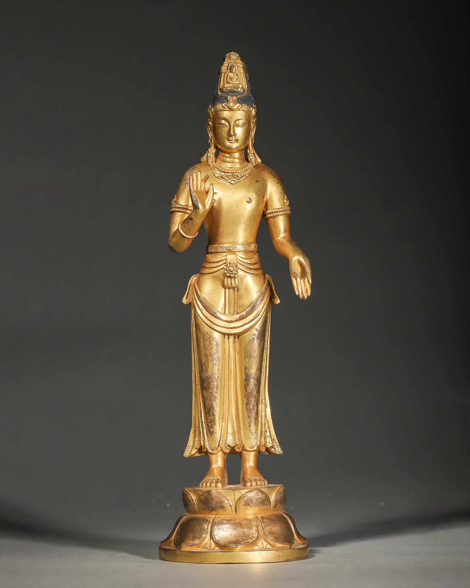 A GILT-BRONZE STANDING FIGURE OF GUANYIN: A gilt-bronze figure of Guanyin standing on a double-lotus base, adorned with jewelry and a crown with a small Buddha figure, the right hand raised in abhaya mudra. L. 10 cm; Ht. 37.5 cm; Wt. 2,692 g.
