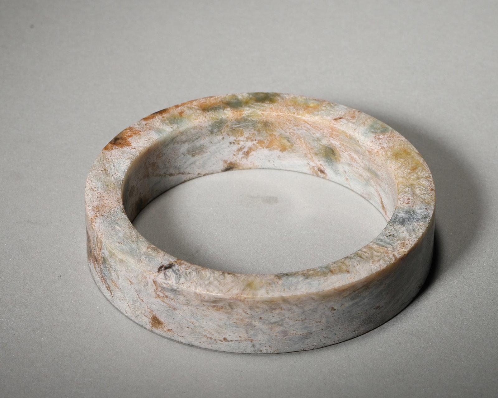 A JADE SQUARE BANGLE, LIANGZHU CULTURE: A jade bangle of broad square section, with calcification and multicolored surface alteration. Diam. 7.5 cm; Inner Diam. 5.8 cm; Wt. 69 g. Note: By repute, associated with Liangzhu culture and with or
