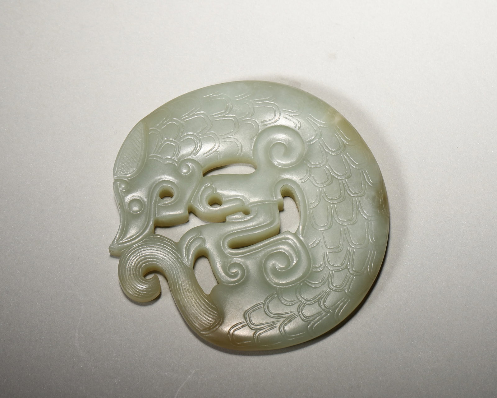 A GREENISH-WHITE JADE OPENWORK 'DOUBLE DRAGON' DISC PENDANT: A greenish-white jade disc pendant carved in openwork with two intertwined dragons, scale and cloud motifs. Diam. 8 cm; Wt. 100 g.