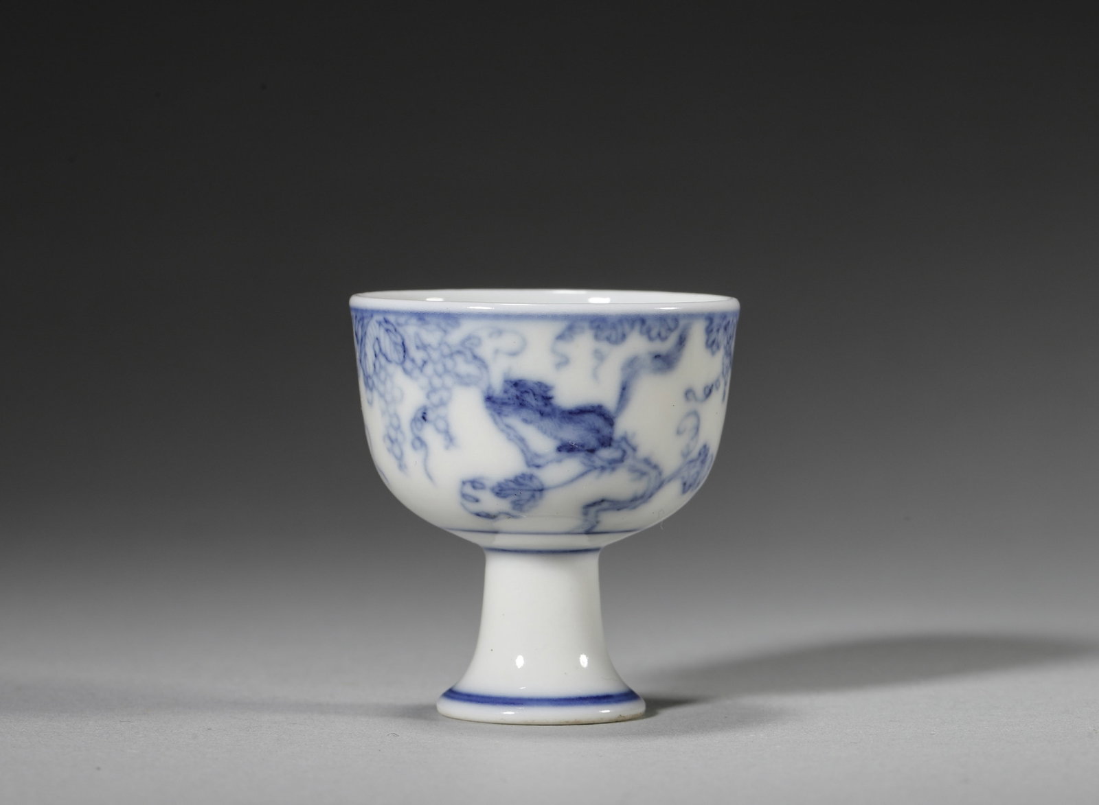 A BLUE-AND-WHITE 'SQUIRREL AND GRAPE' MINIATURE STEM CUP: A miniature blue-and-white stem cup decorated with squirrels and grapes. The base bears a mark reading 'Yongzheng'. Diam. 3.5 cm; Ht. 4 cm.