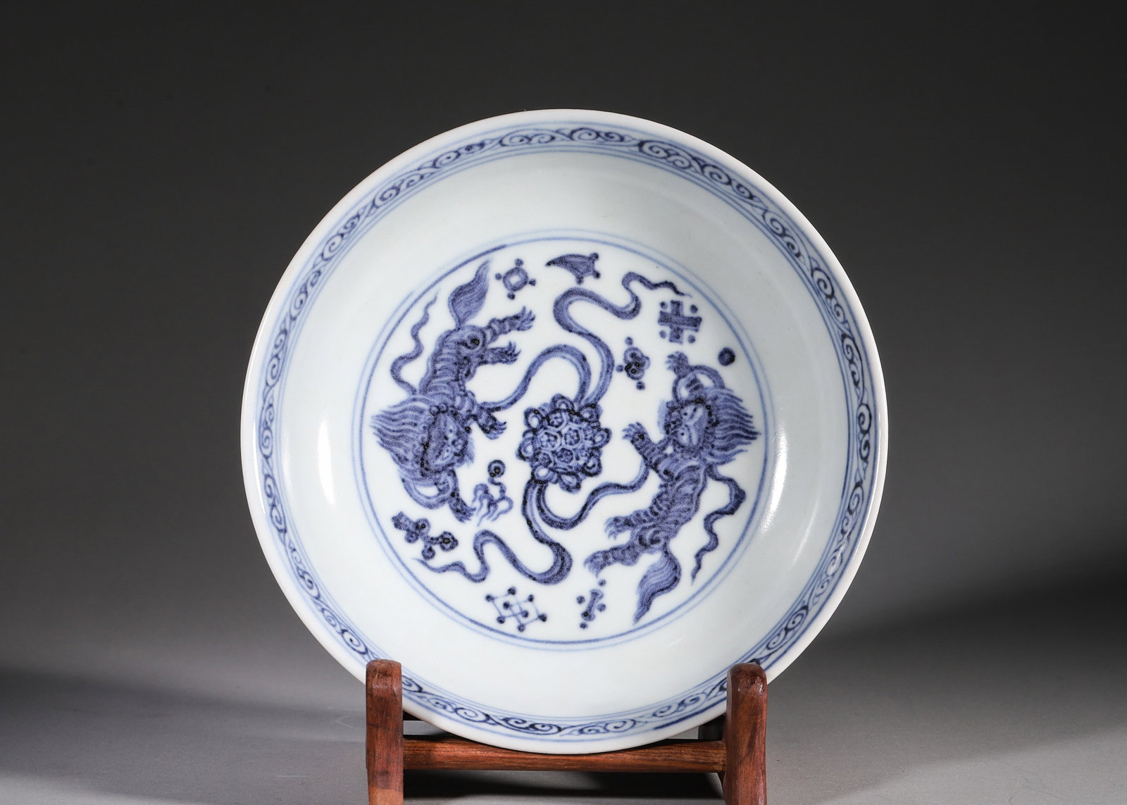 A BLUE-AND-WHITE FOLIATE-RIM DISH WITH TWIN LIONS AND TREASURES: A blue-and-white shallow dish with a foliate rim, the interior decorated with twin lions and a floral ball surrounded by auspicious treasures, with scrolling decoration to the rim and exterior. The