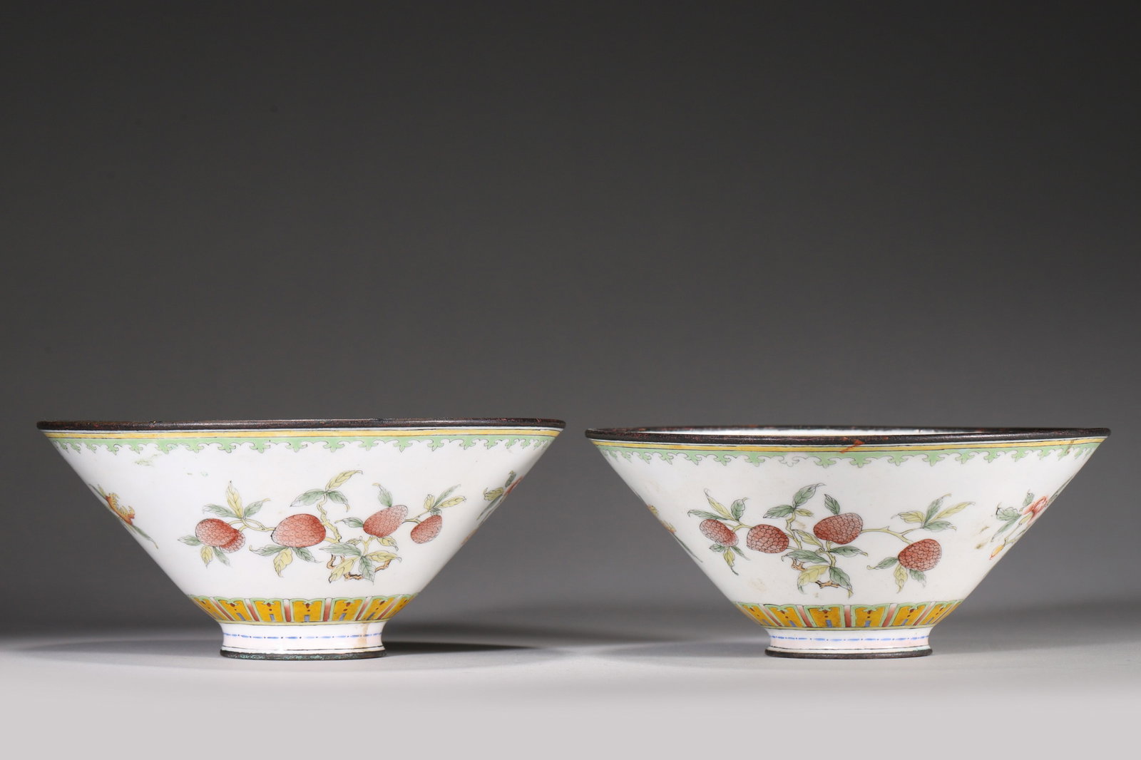 A PAIR OF COPPER-BODY PAINTED-ENAMEL 'THREE ABUNDANCES' BOWLS: A pair of conical copper-body painted-enamel bowls with copper-bound rims, the exteriors decorated with pomegranates, peaches and citrons on a white ground, and the interiors with figures of the Eight