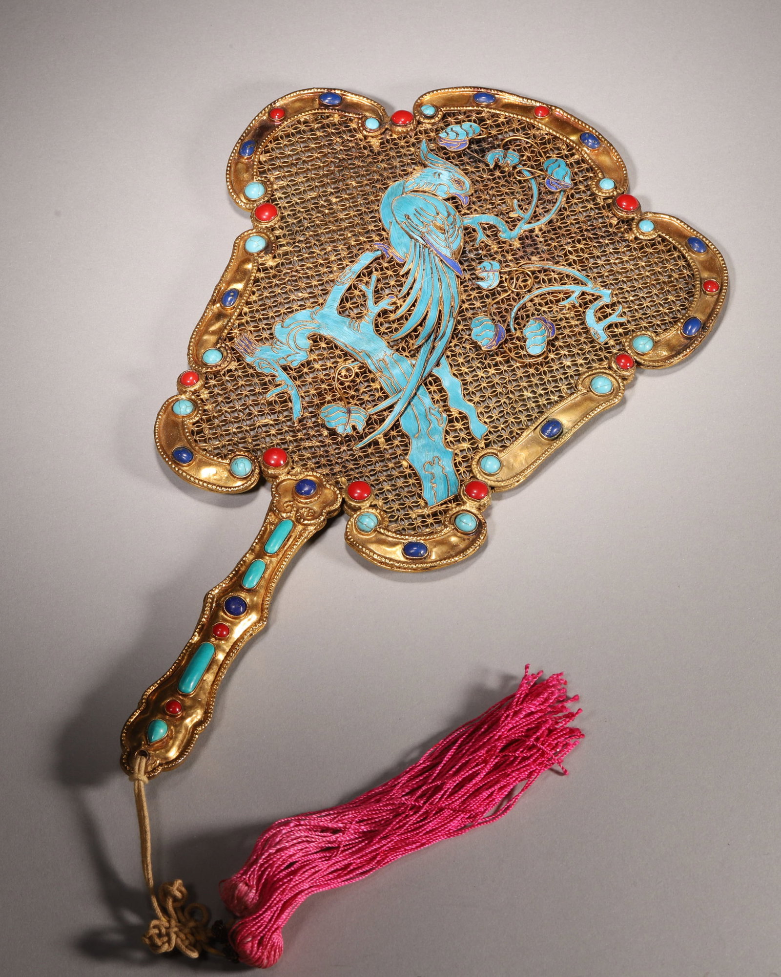 A GILT-BRONZE FILIGREE FAN WITH KINGFISHER-FEATHER AND GEM INLAY: A gilt-bronze filigree fan decorated with kingfisher-feather bird-and-flower motifs and set with red coral, lapis lazuli and turquoise along the edge and handle. L. 30 cm; W. 18 cm; Wt. 314 g.