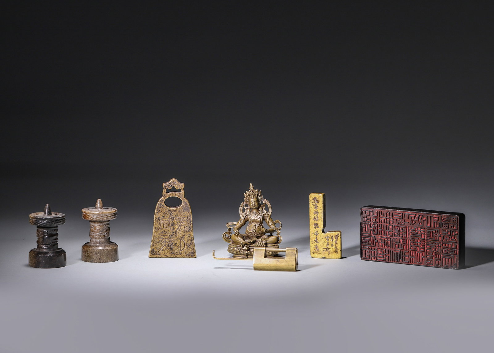 A SET OF SIX BRONZE AND STONE RITUAL AND SCHOLAR'S OBJECTS: A set of six bronze and stone objects comprising a pair of stone ritual seals, a bell-form bronze tally, a bronze Bodhisattva figure, a bronze lock and a rectangular carved seal. Largest: L. 10 cm; W.
