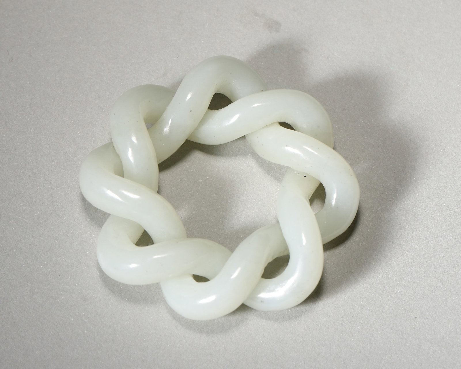 A WHITE JADE INTERLOCKING-KNOT PENDANT: A white jade pendant carved from a single piece as an interlocking knot. Diam. 5 cm; Wt. 38 g. Note: The interlocking-knot form is traditionally associated with enduring union.