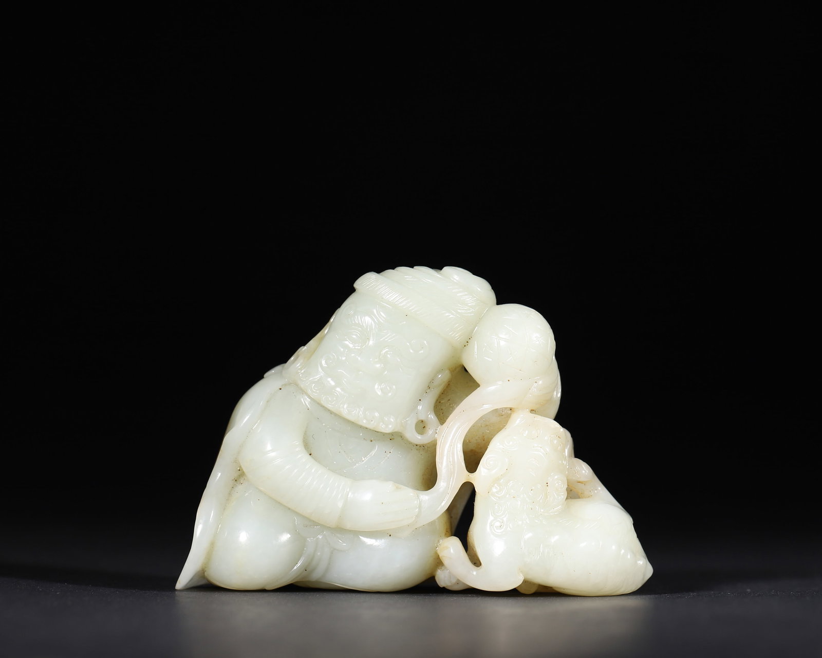 A WHITE JADE 'FOREIGNER AND LION' GROUP: A white jade group carved in the round with a foreign figure and a lion, with areas of russet skin. L. 8.5 cm; W. 5.5 cm; Wt. 186 g.
