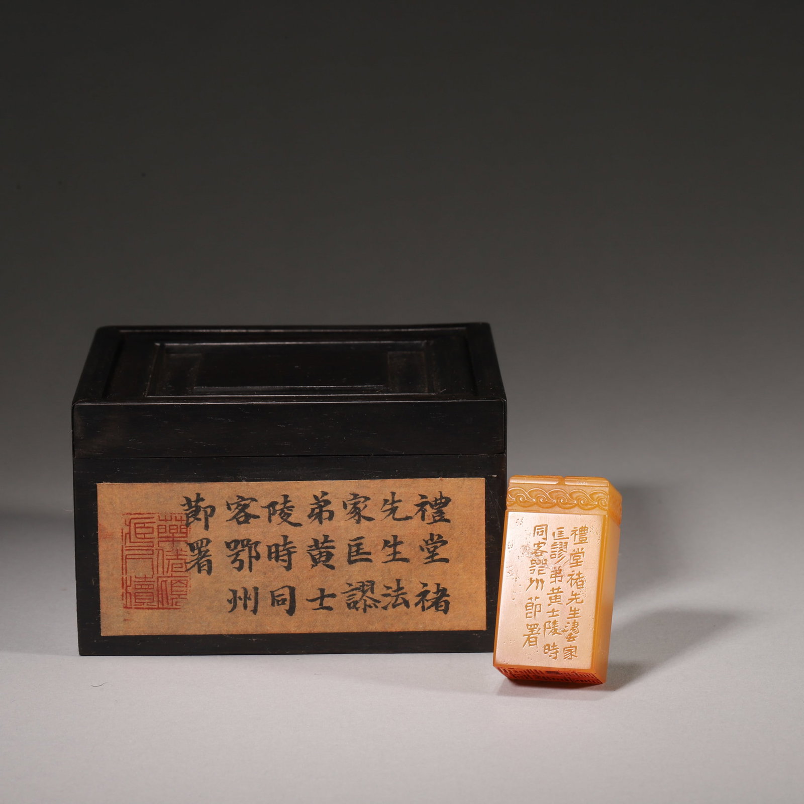 A YELLOW STONE SEAL WITH ARCHAISTIC DRAGON KNOB: A square yellow stone seal carved with an archaistic dragon-scroll knob and wave motifs. The side bears an inscription referring to Huang Shiling, and the base is carved with seal-script characters. L