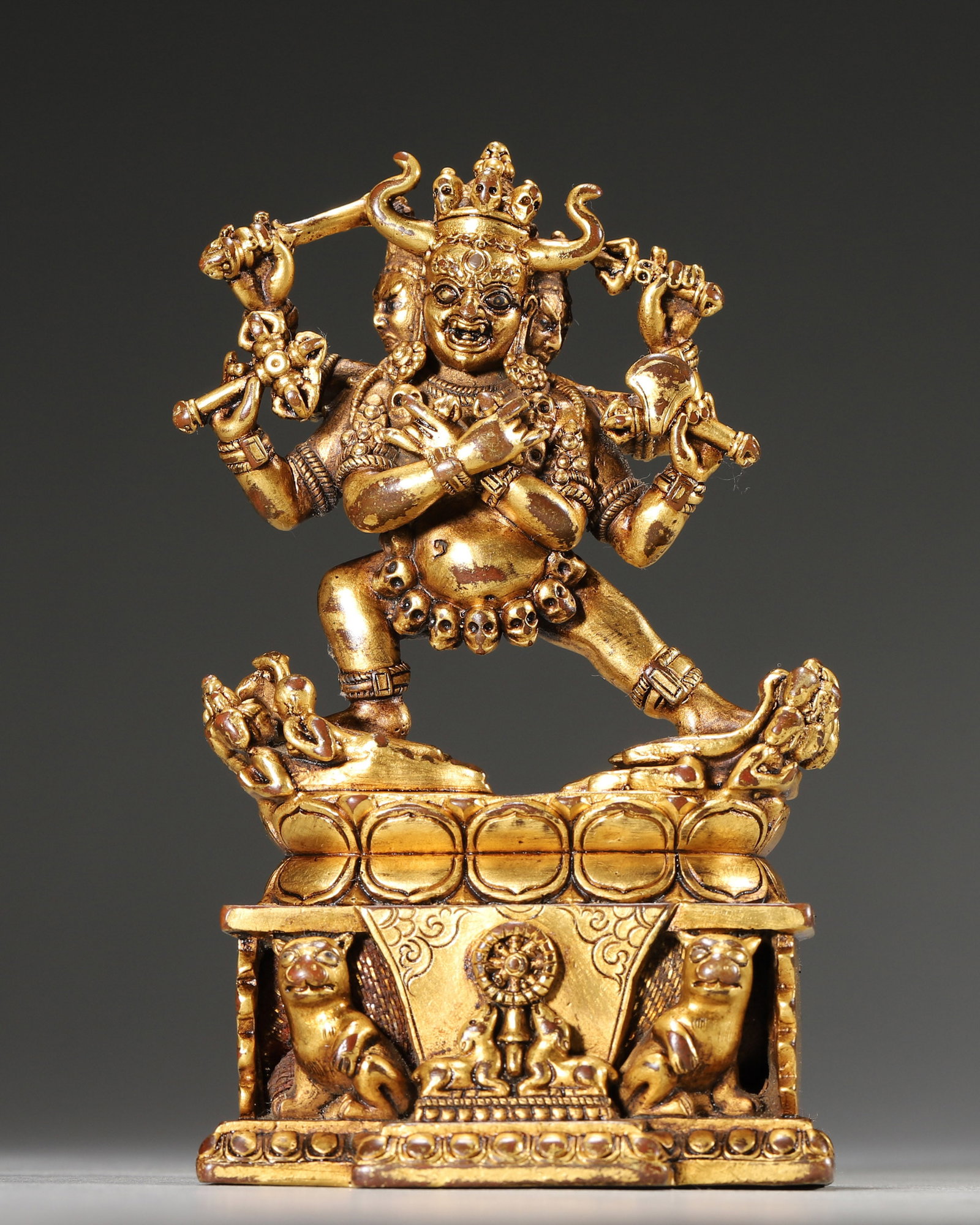 A GILT-BRONZE YAB-YUM GUARDIAN DEITY GROUP: A gilt-bronze multi-headed and multi-armed guardian deity group in yab-yum, holding ritual implements and standing above prostrate figures, with skull ornaments and decorative motifs to the pedestal. 