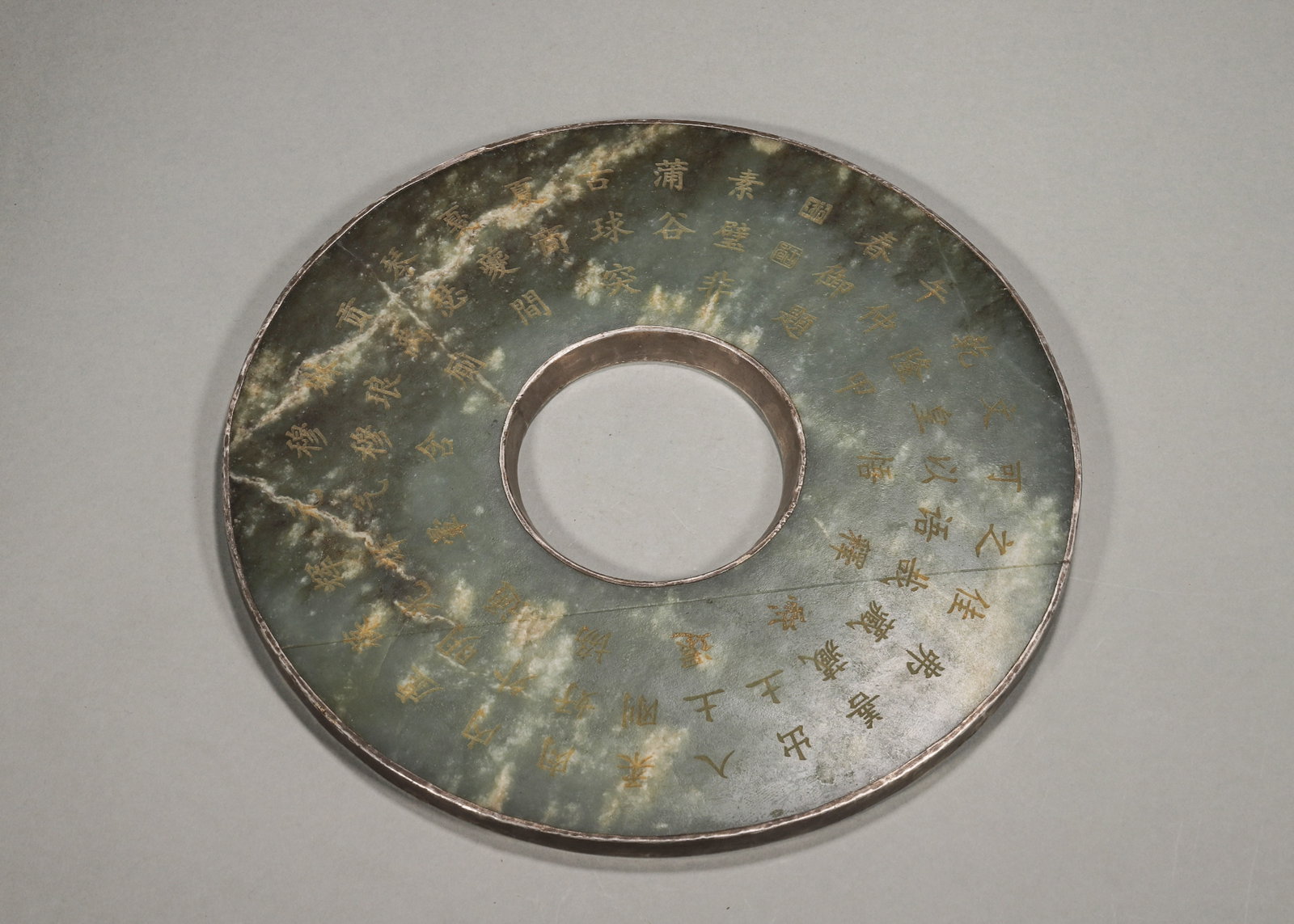 A JASPER BI WITH GILT INSCRIPTION AND SILVER MOUNT: A jasper bi mounted with a silver rim, one side bearing a gilt inscription and the reverse fitted with a silver casing engraved with beasts. W. 22.3 cm; Wt. 1,059 g. Note: By repute, associated with