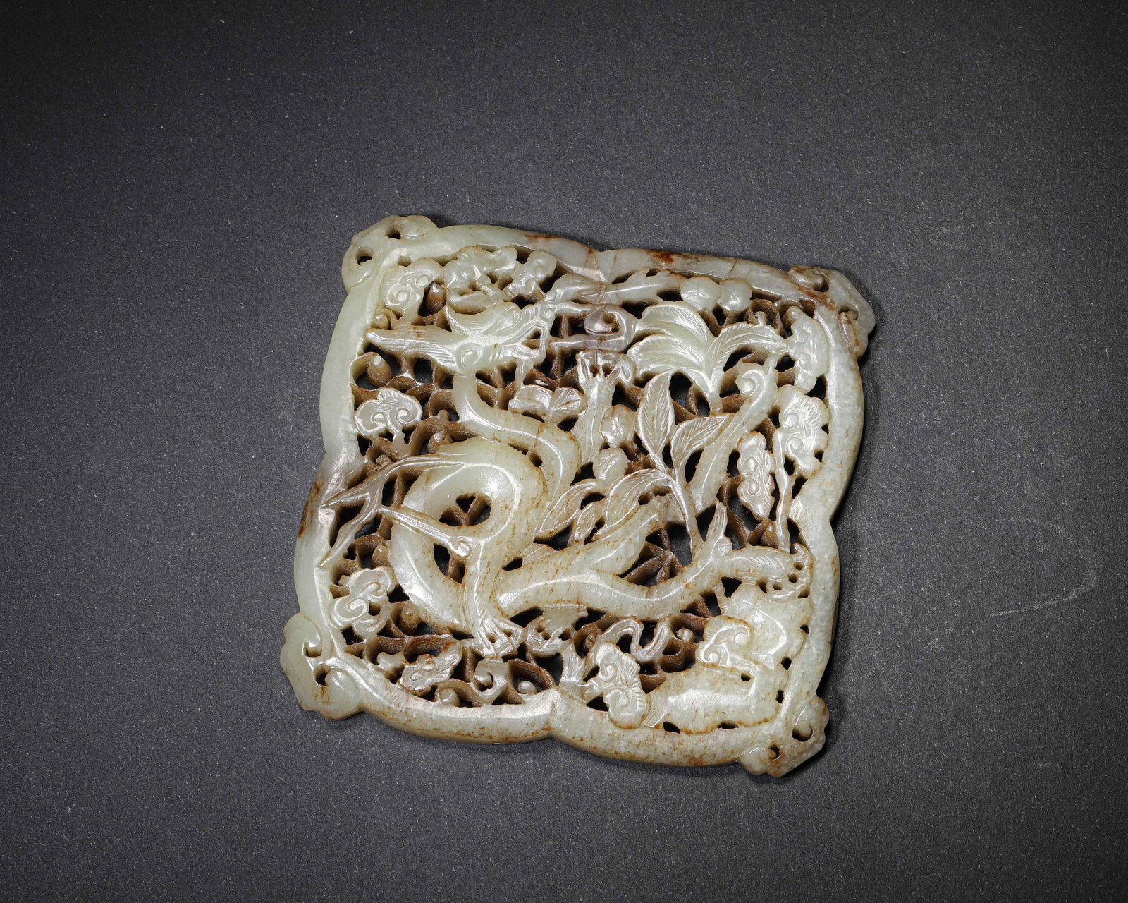 A JADE OPENWORK 'DRAGON AND LINGZHI' BELT PLAQUE: A jade belt plaque carved in openwork with a dragon, lingzhi and additional beast motifs. L. 10 cm; W. 9.4 cm; Wt. 203 g.