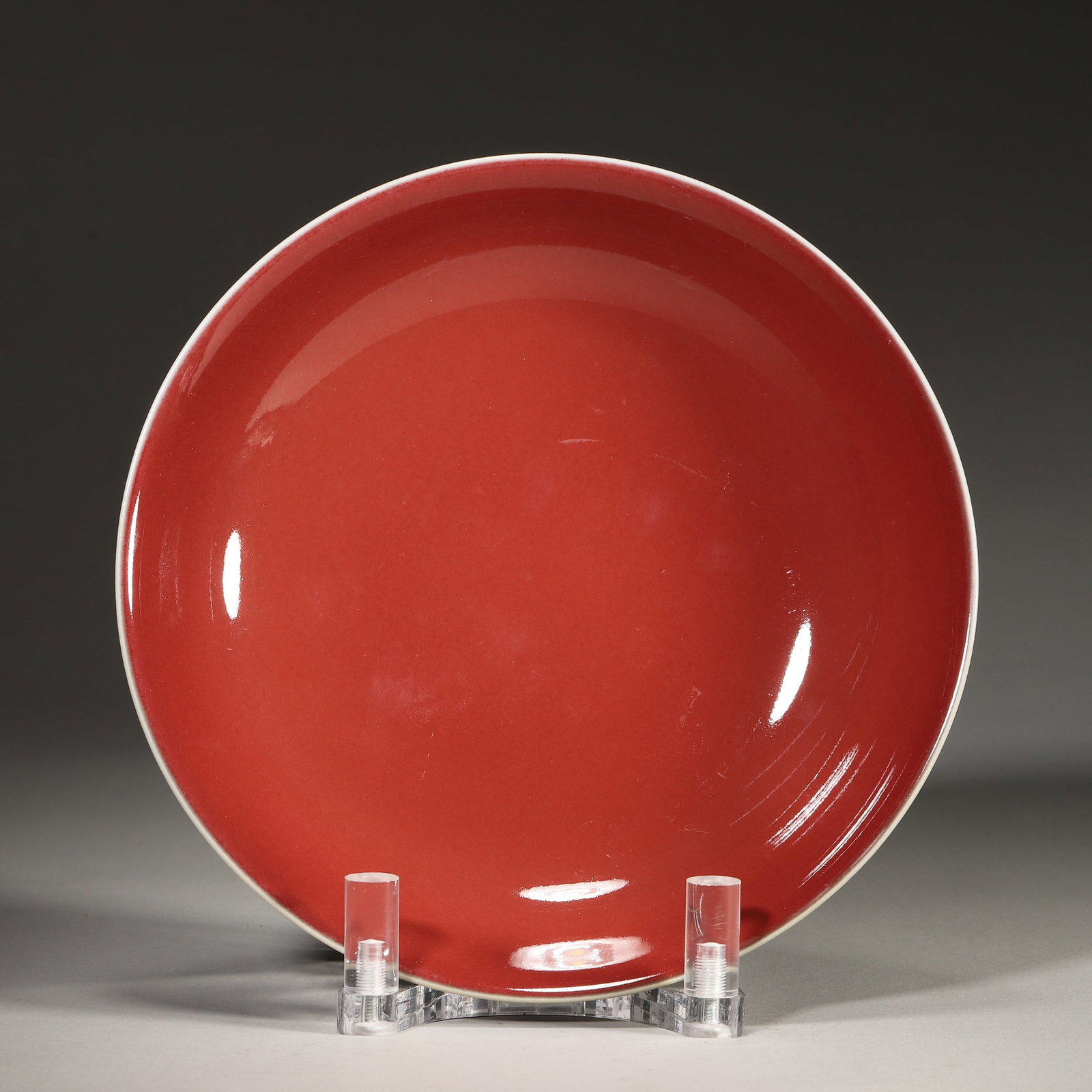 A COPPER-RED-GLAZED DISH: A porcelain dish covered in a copper-red glaze. The base bears a six-character mark within a double circle. Diam. 19 cm; Ht. 4.5 cm. Note: By repute, previously associated with sales at Bonhams and Ch