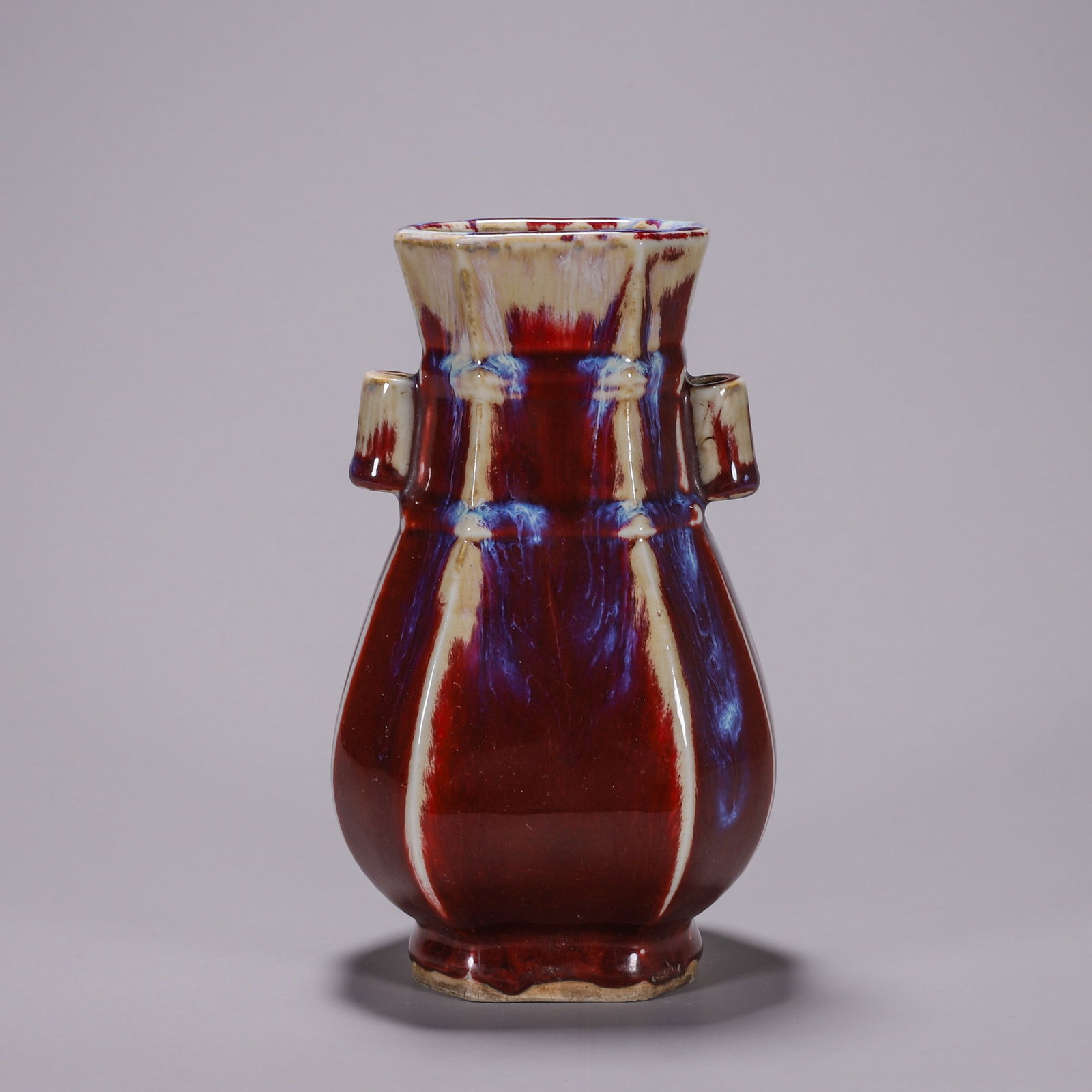 A FLAMBE-GLAZED OCTAGONAL VASE WITH PIERCED HANDLES: An octagonal porcelain vase with double pierced handles, covered in a flambe glaze of red with blue-purple streaks. L. 11 cm; W. 9 cm; Ht. 18 cm.