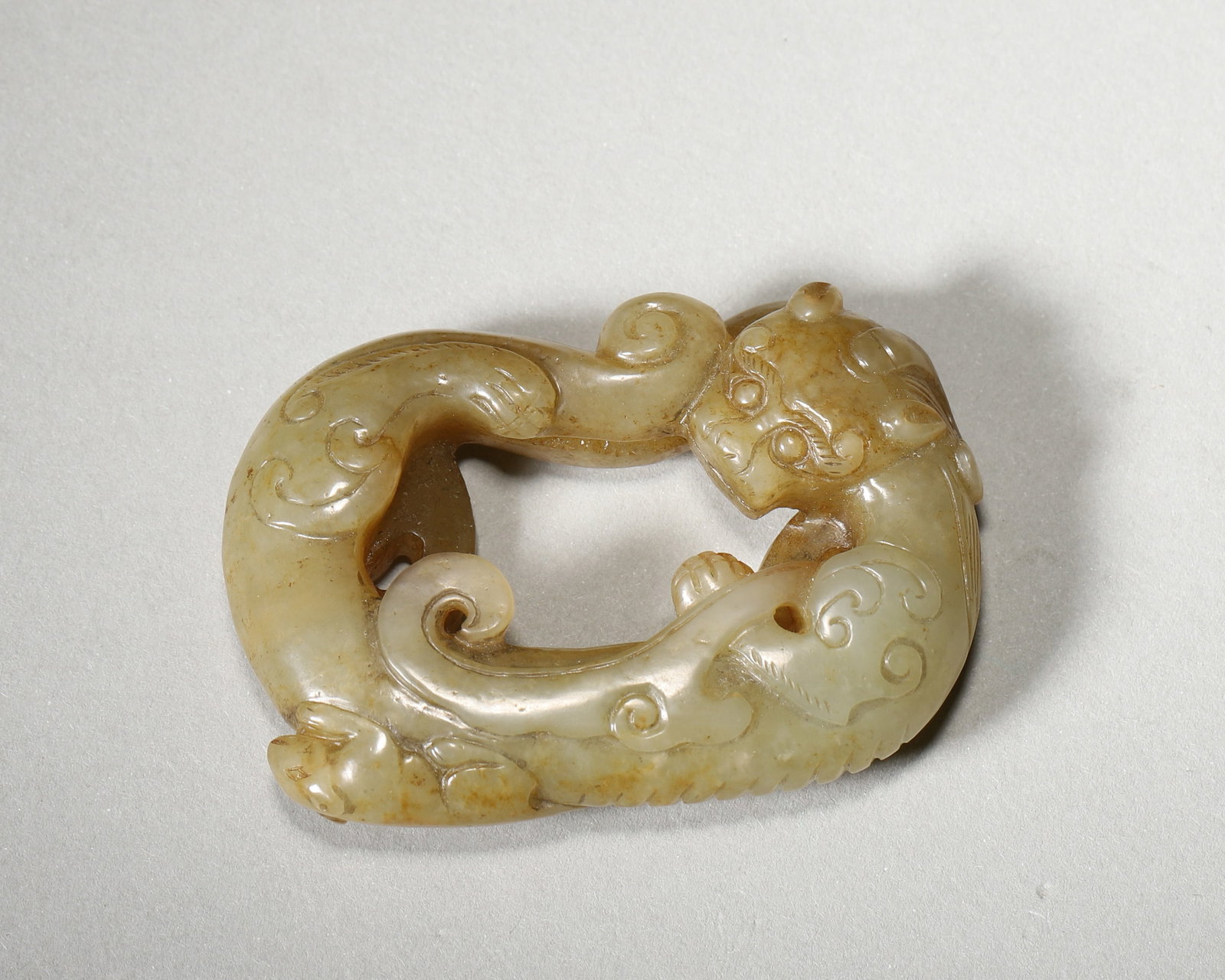 A JADE COILED-CHILONG PENDANT: A jade pendant carved in openwork with a coiled chilong. L. 5.5 cm; W. 4 cm; Wt. 47 g. Note: By repute, associated with personal adornment and protective symbolism.