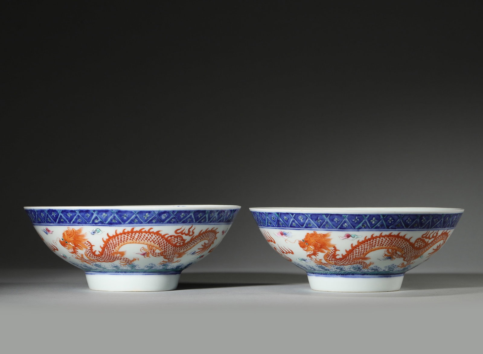 A PAIR OF BLUE-AND-WHITE AND IRON-RED 'DRAGON' BOWLS: A pair of porcelain bowls decorated with iron-red dragons, clouds and waves, with blue-and-white borders at the rims. The bases bear marks in the name of Guangxu. Each: Diam. 16 cm; Ht. 6 cm.