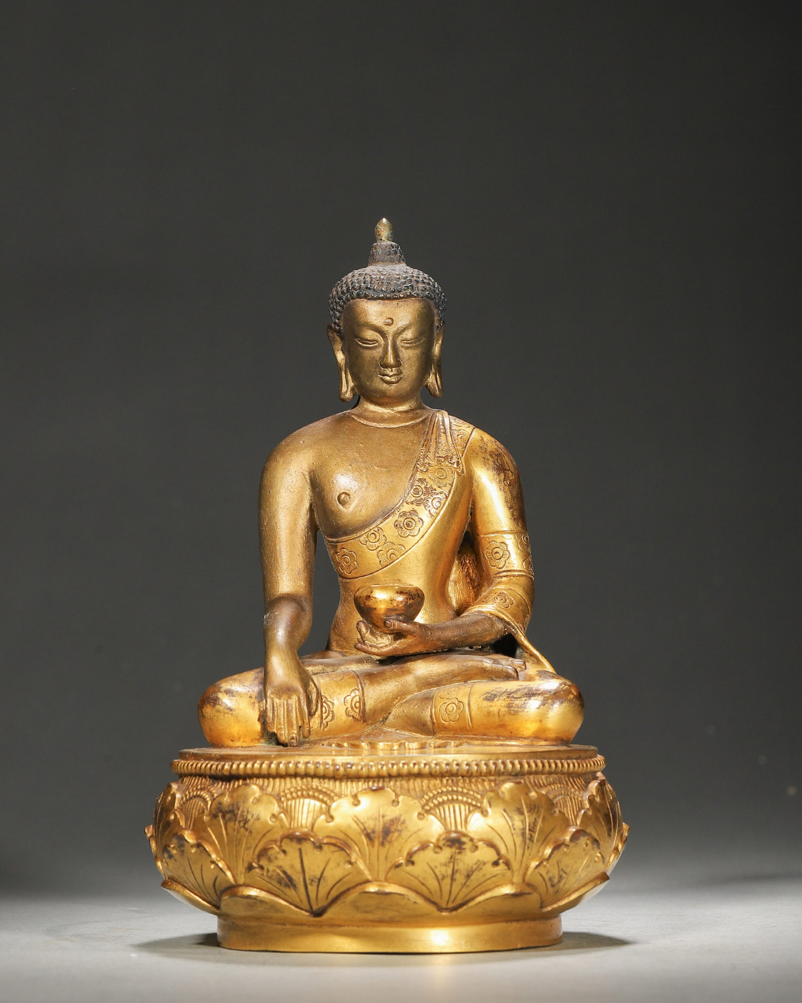 A GILT-BRONZE FIGURE OF SHAKYAMUNI BUDDHA: A gilt-bronze figure of Shakyamuni Buddha seated on a lotus base. W. 11 cm; Ht. 18 cm; Wt. 1,412 g.
