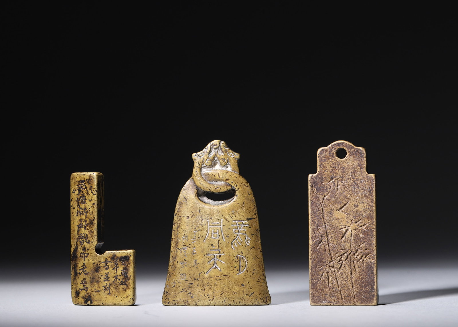 A SET OF THREE BRONZE INSCRIBED SCHOLAR'S OBJECTS: A set of three bronze scholar's objects comprising an L-shaped inscribed seal, a dragon-headed bell-form tally and a rectangular plaque carved with bamboo. Largest: L. 4.8 cm; Ht. 7.3 cm; Total Wt.