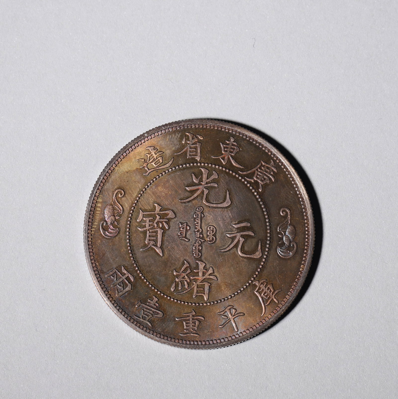 A 'GUANGXU YUANBAO' DOUBLE-DRAGON 'SHOU' SILVER COIN: A silver coin bearing inscriptions including 'Guangxu Yuanbao' and 'Guangdong Province', with bat motifs to the obverse and a central 'Shou' motif with confronting dragons to the reverse. Diam. 4.4
