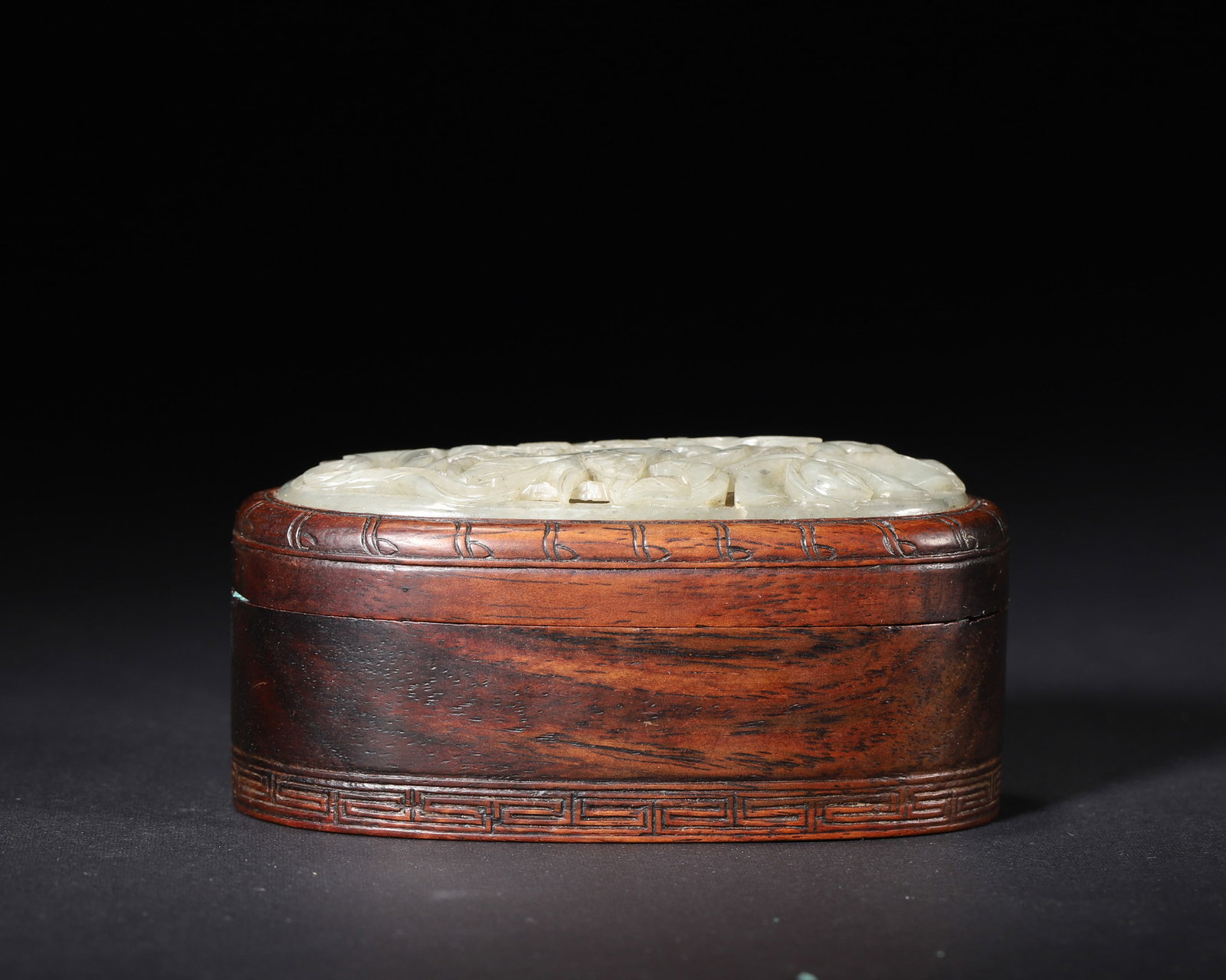 A HUANGHUALI BOX WITH WHITE JADE OPENWORK 'BIRD AND FLOWER' COVER: A huanghuali wood box with a white jade openwork cover carved with bird-and-flower motifs, with key-fret and bamboo decoration. L. 9.5 cm; W. 5 cm; Ht. 5 cm; Wt. 123 g.
